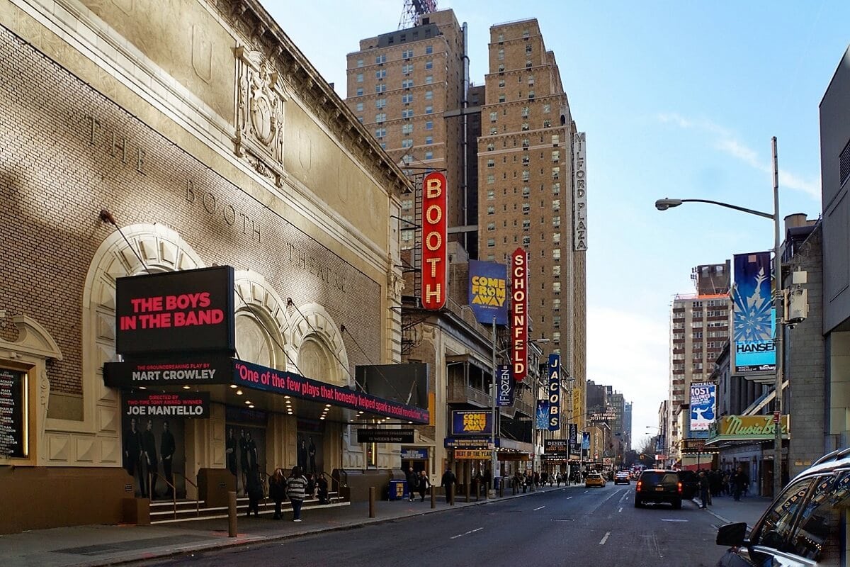 A view of the Booth Theatre on Broadway in New York City, showcasing the marquee for 'The Boys in the Band' and other surrounding theaters and buildings