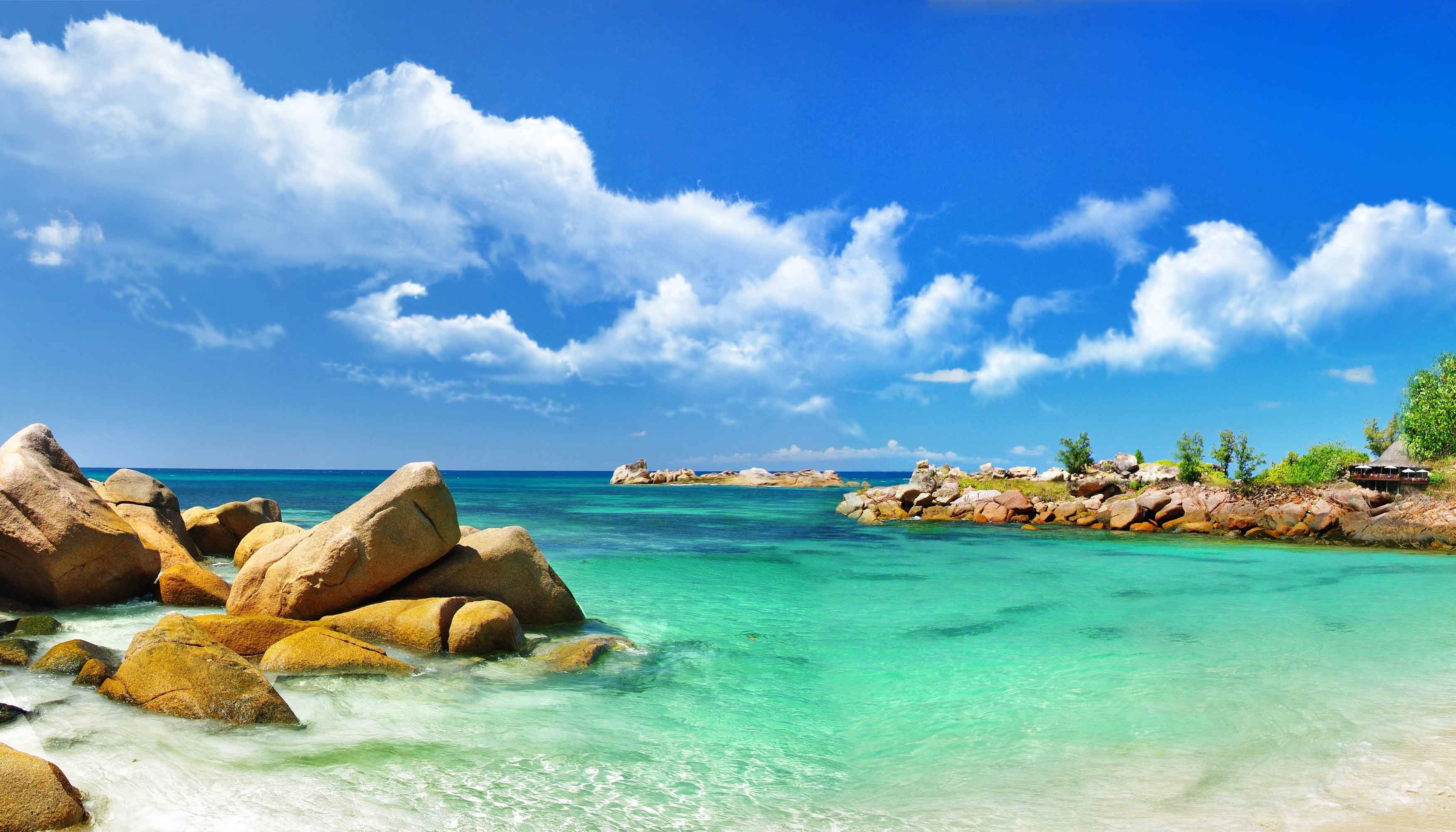 Tropical beach paradise with turquoise water, granite boulders, and lush vegetation under a sunny sky