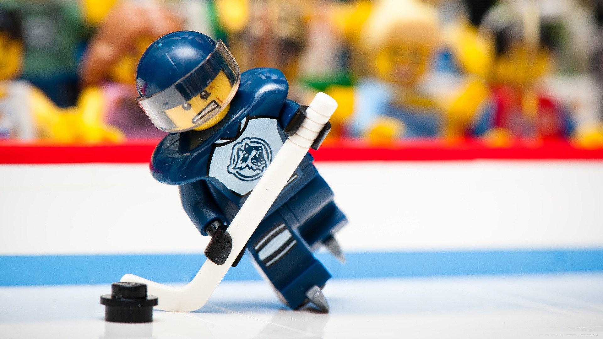 Lego hockey player about to strike the puck on the ice, in front of a blurred crowd