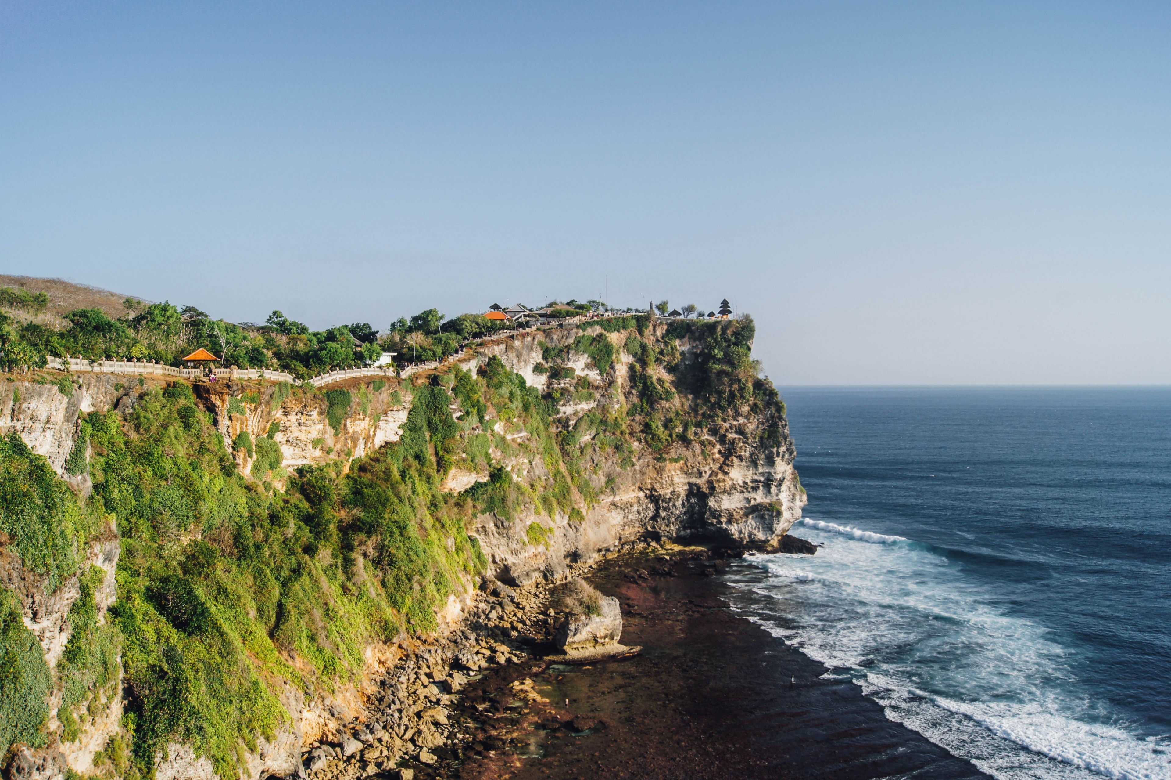 A breathtaking 4k wallpaper showcasing a lush green cliff overlooking a deep blue ocean, with a traditional Balinese temple perched on the edge