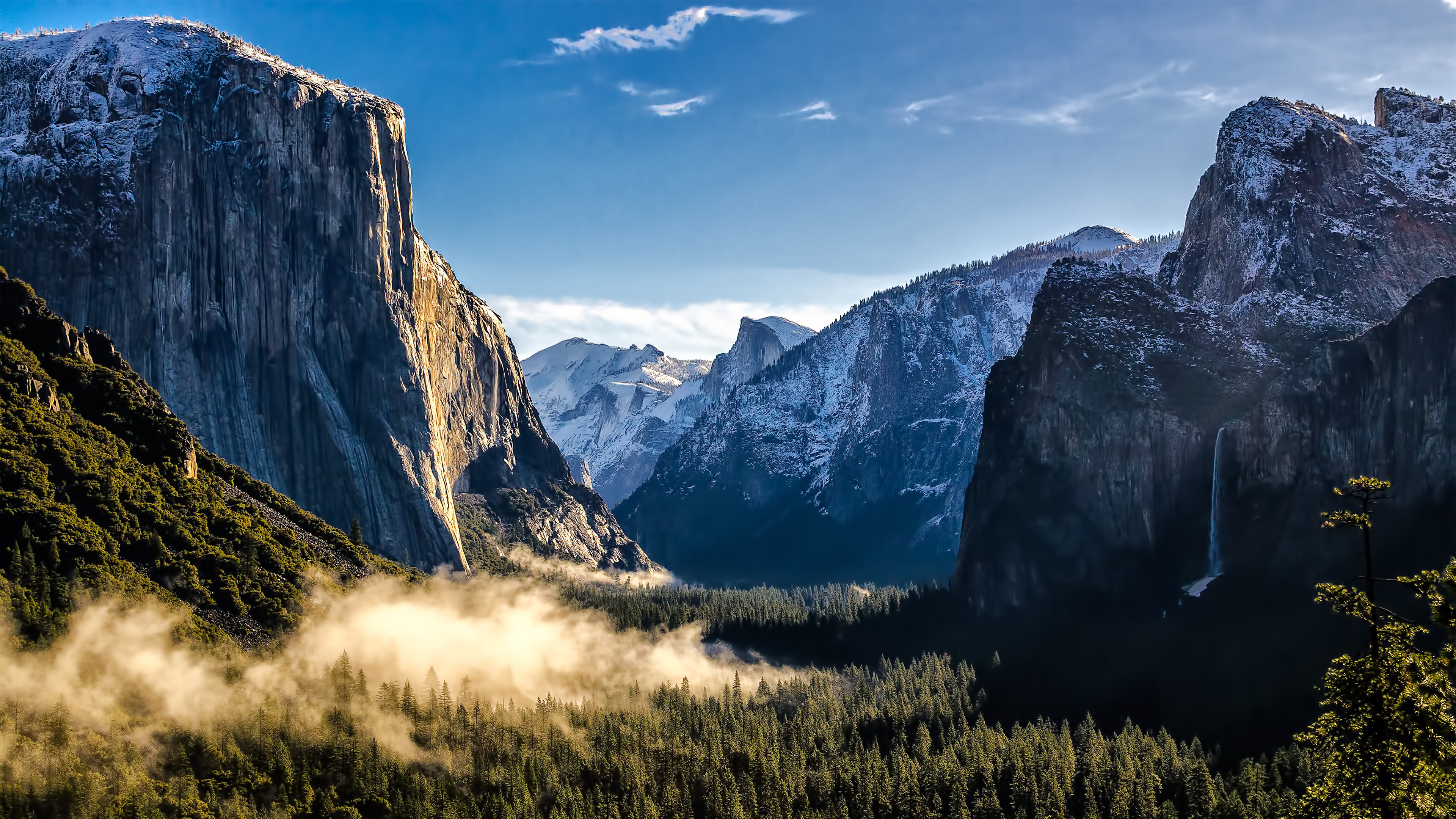 4K wallpaper of a breathtaking vista of Yosemite Valley, featuring iconic granite cliffs, a cascading waterfall, and a misty forest floor