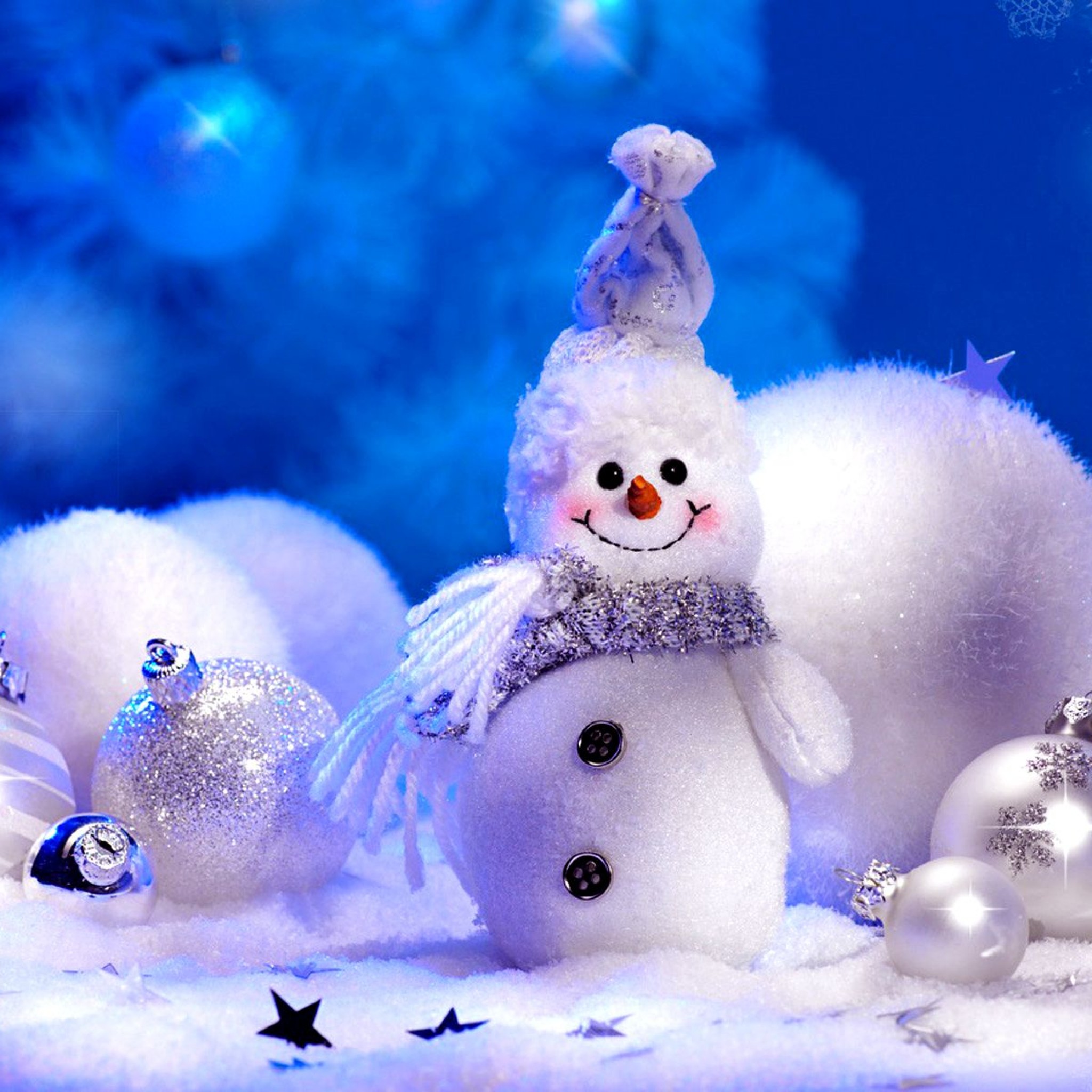 A cheerful snowman ornament nestled in the snow amidst silver and white Christmas ornaments, set against a backdrop of sparkling blue Christmas lights
