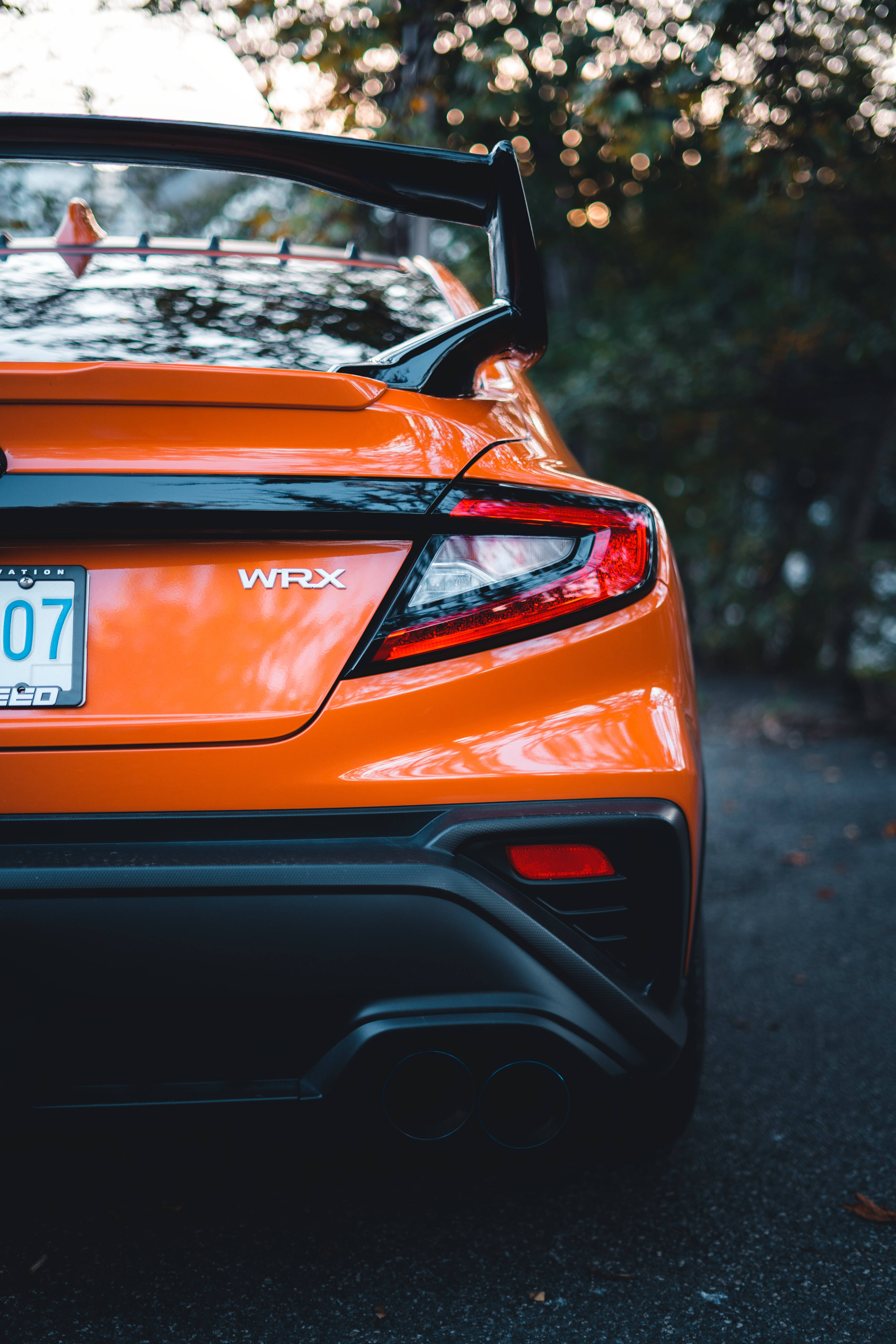 Rear view of a bright orange Subaru WRX sports car parked on asphalt, showcasing its spoiler, taillights, and dual exhaust pipes
