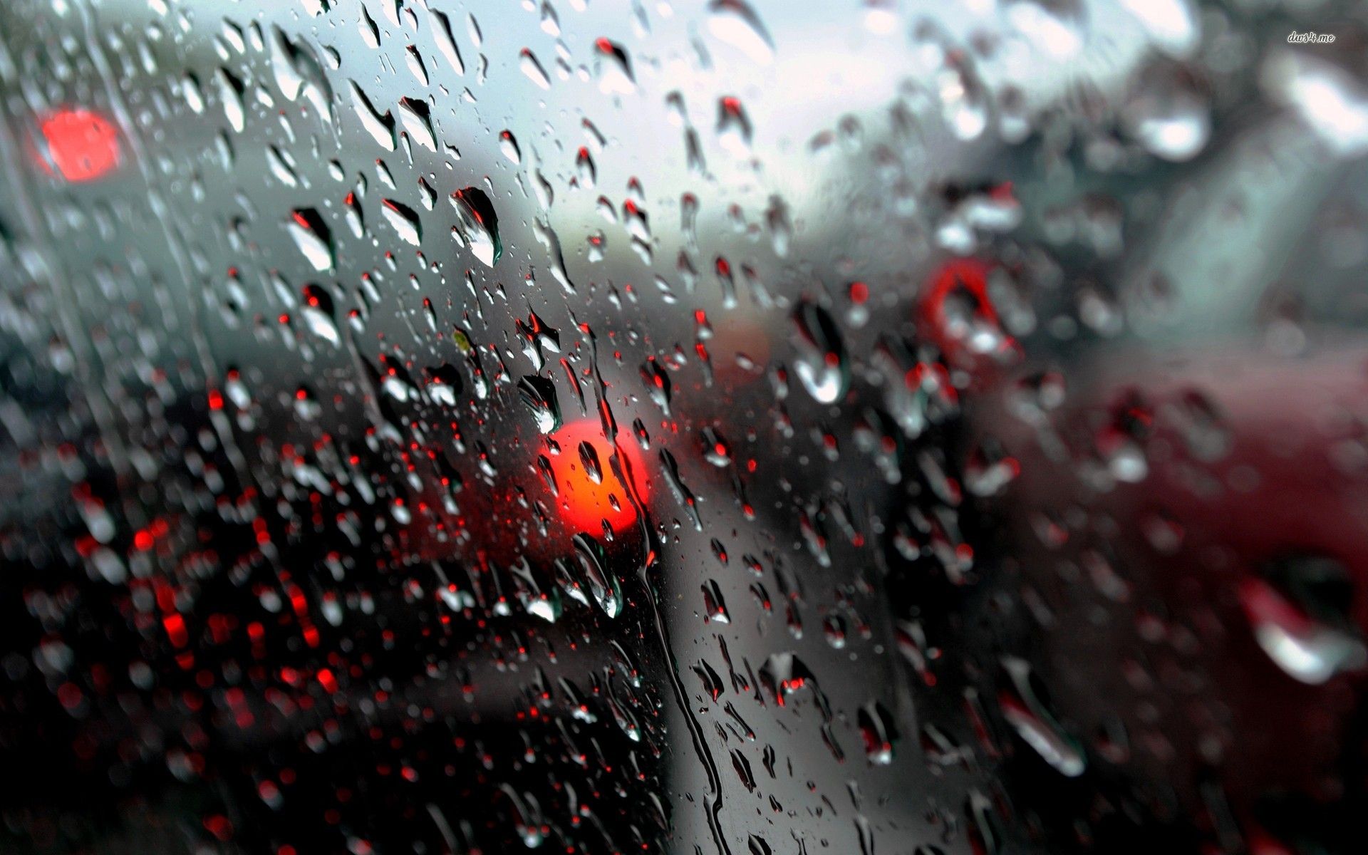 Raindrops on a car window with blurred red lights in the background, creating a moody and atmospheric rainy day scene