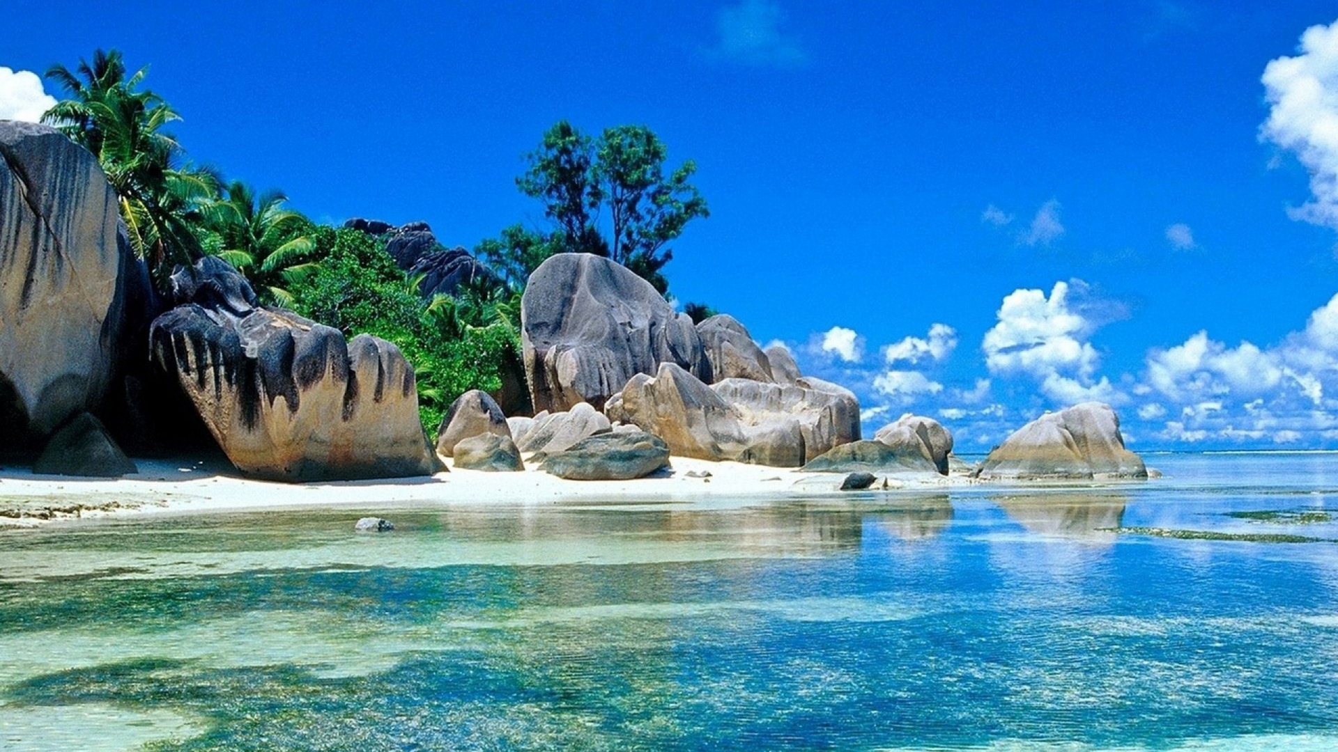 Tropical beach paradise with crystal-clear turquoise water and granite boulders under a sunny blue sky