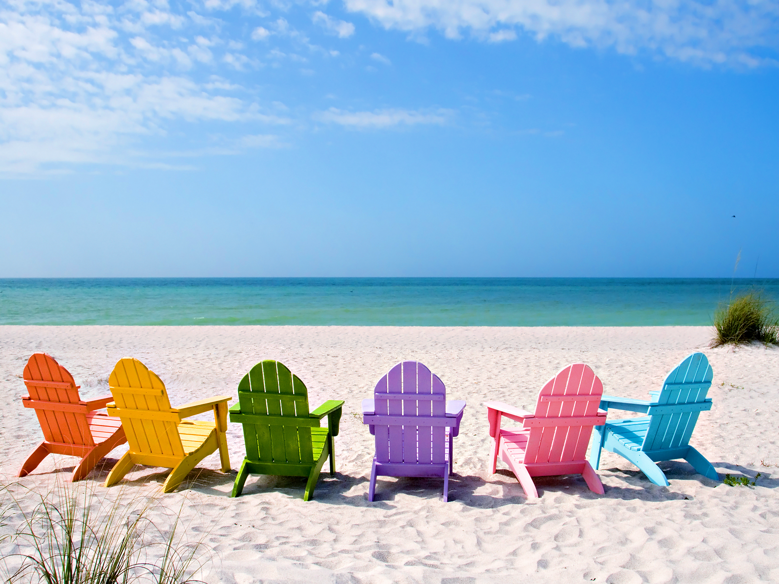 Vividly colored beach chairs lined up on a white sandy beach overlooking a tranquil turquoise ocean under a bright blue sky, evoking a perfect summer vacation