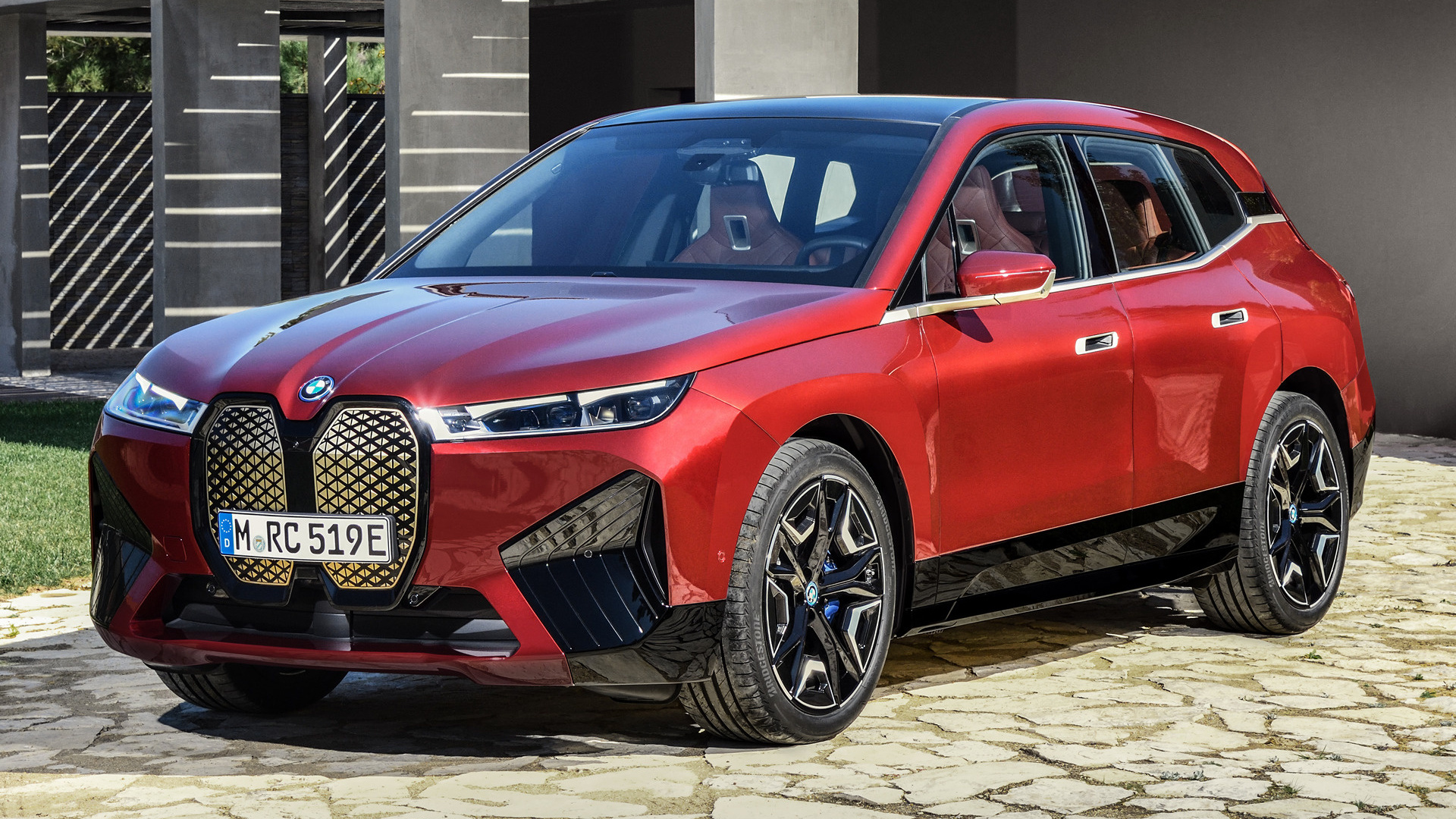 A red BMW iX electric SUV parked in front of a modern house