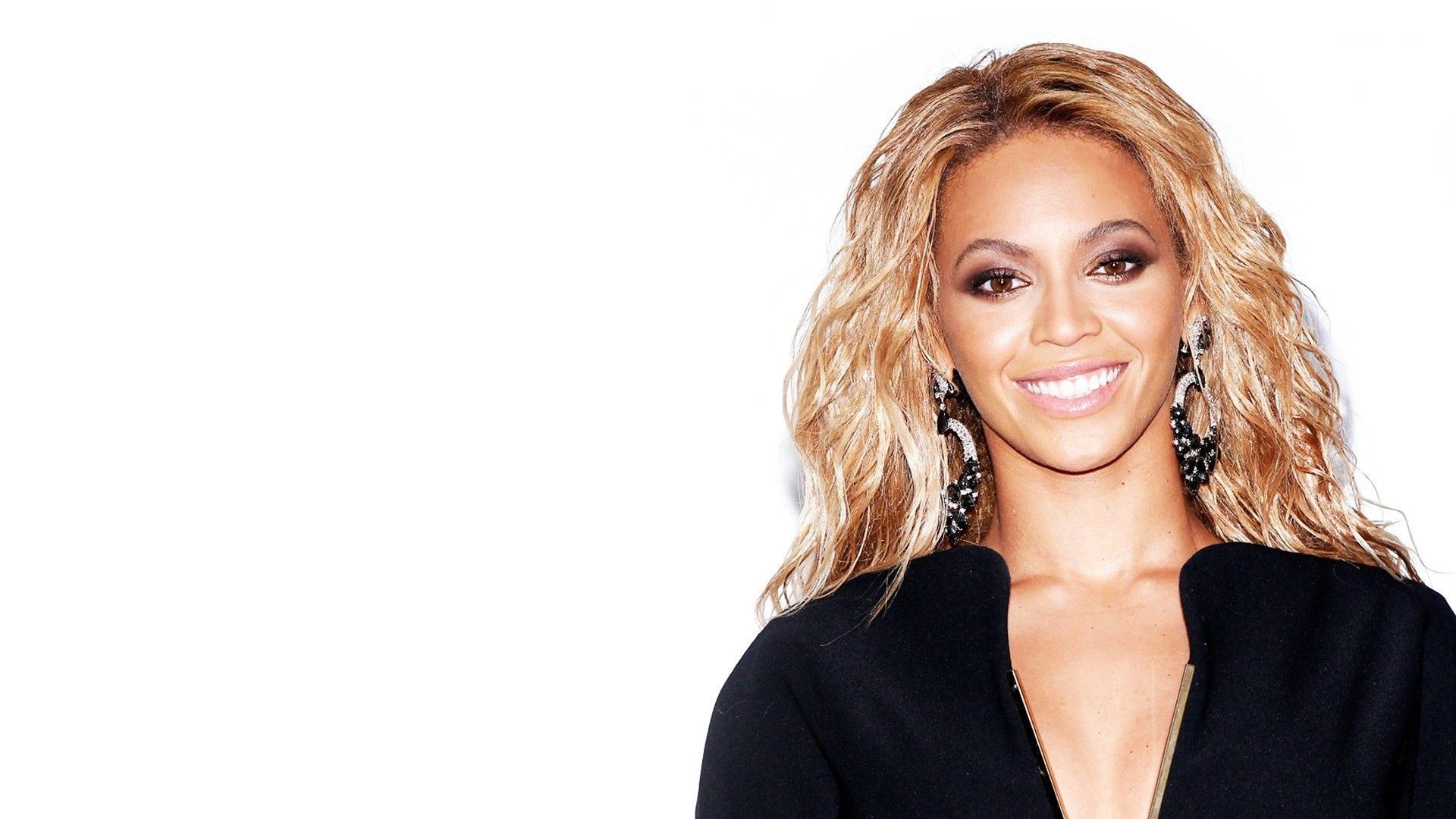 Beyoncé Knowles-Carter, a pop icon, smiles at the camera while wearing a stylish black top against a minimalist white backdrop