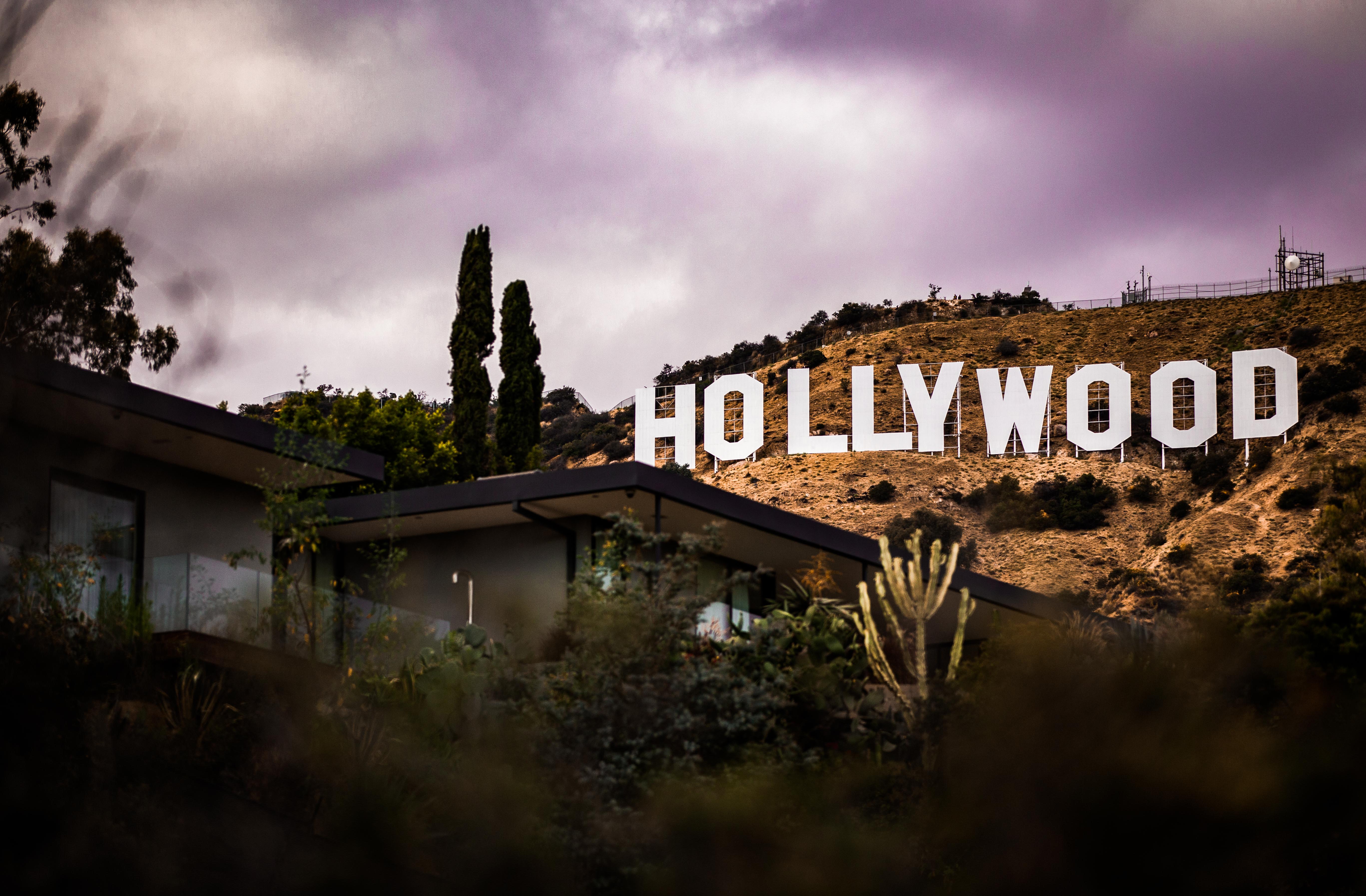 The iconic Hollywood Sign stands tall against a dramatic, cloud-filled sky, viewed from a hillside residence