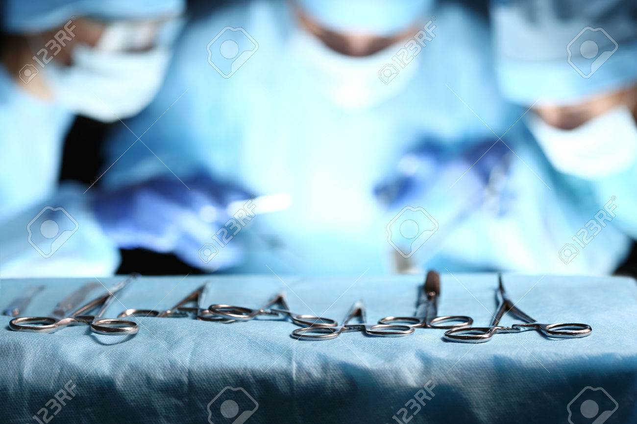 Surgical Tools Lying On Table Wile Group Of Surgeons At Background