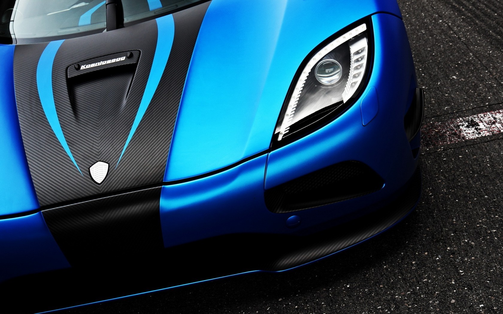 Close-up of a blue Koenigsegg Agera sports car with black accents, parked on a racetrack