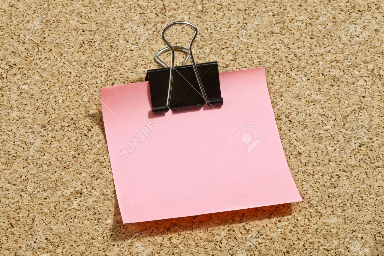 Pink Memo Note With Black Binder Clip Over A Cork Board Background