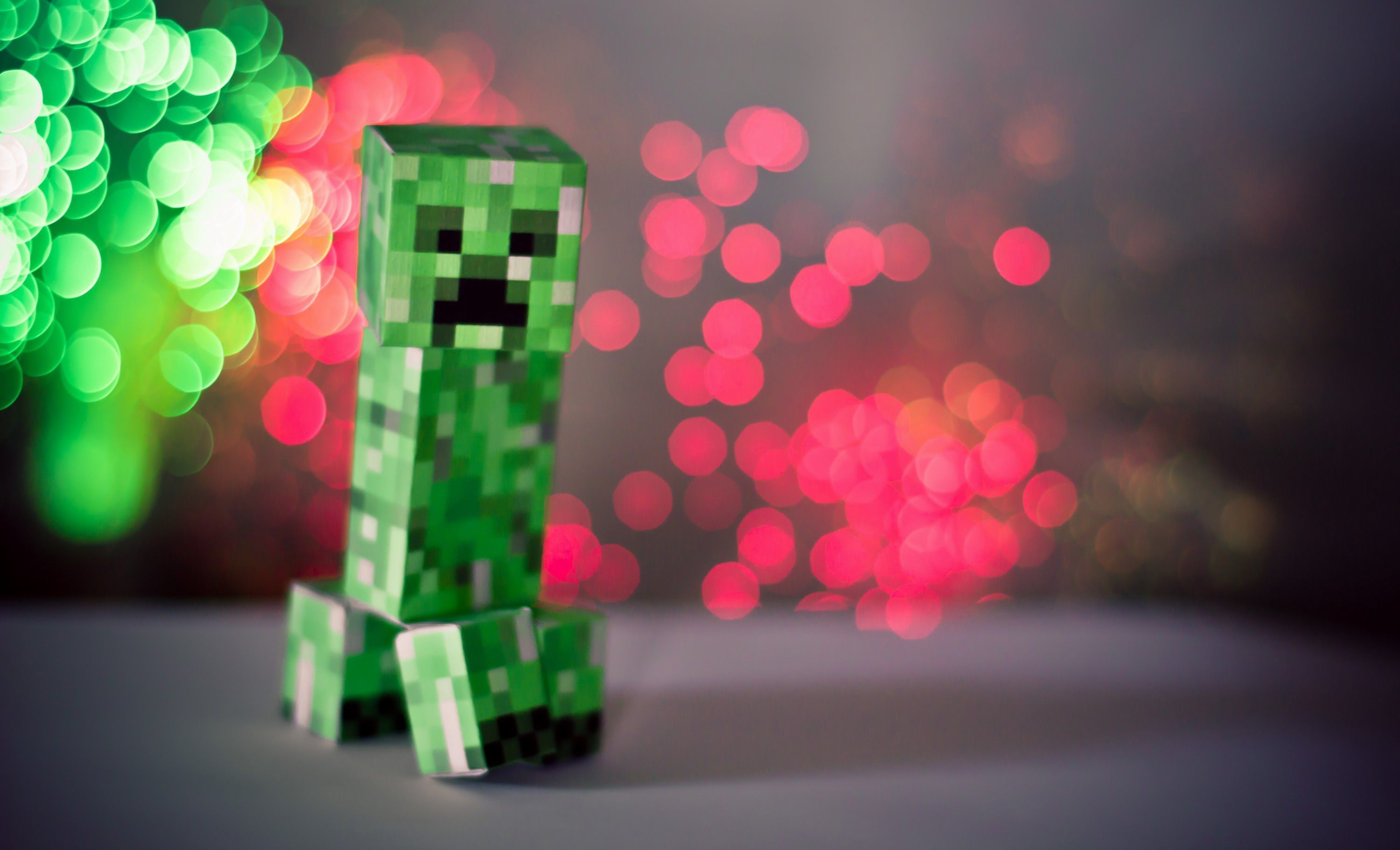 A papercraft Creeper figure stands against a festive bokeh background of green and red lights, a whimsical representation of the popular Minecraft video game