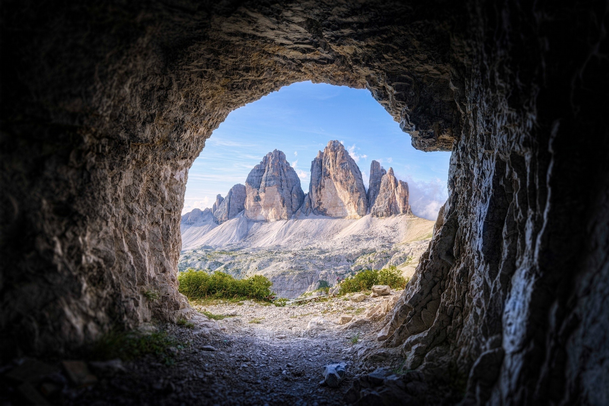 A breathtaking view of the Tre Cime di Lavaredo peaks through the opening of a dark cave, showcasing the beauty of the Dolomites