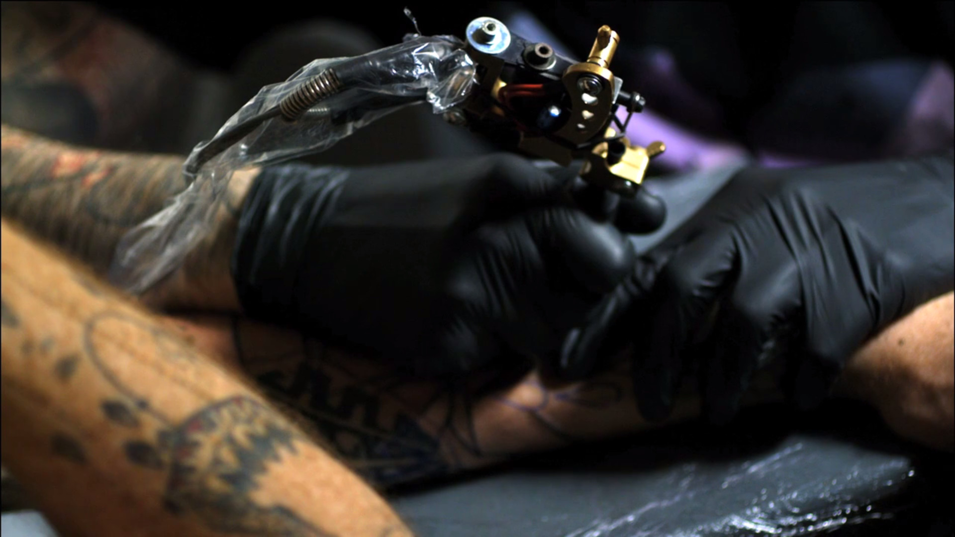 Close-up of a tattoo artist's gloved hands applying a tattoo on a person's arm