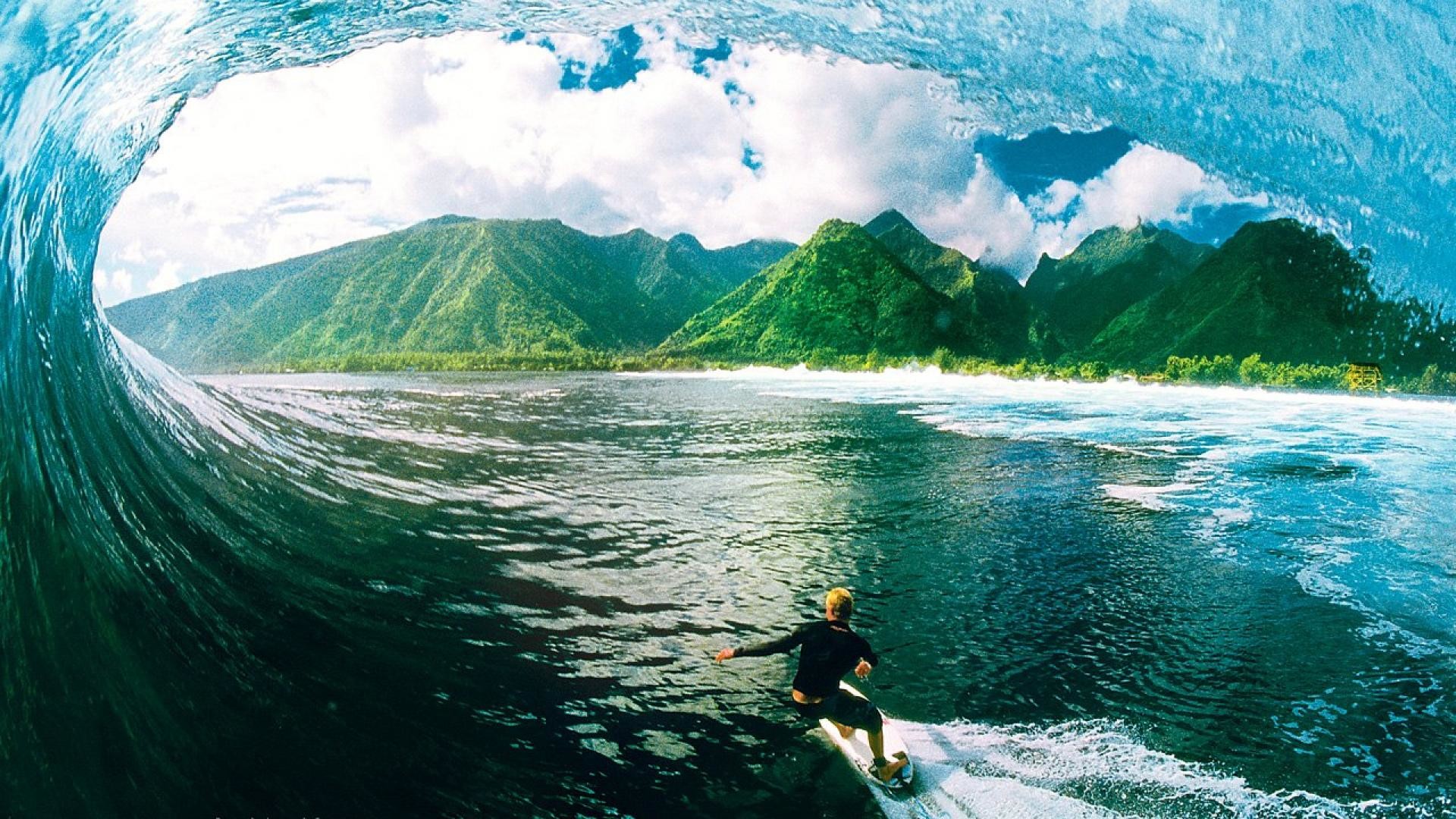 A surfer riding a wave with lush green mountains in the background, Surfing Wallpaper