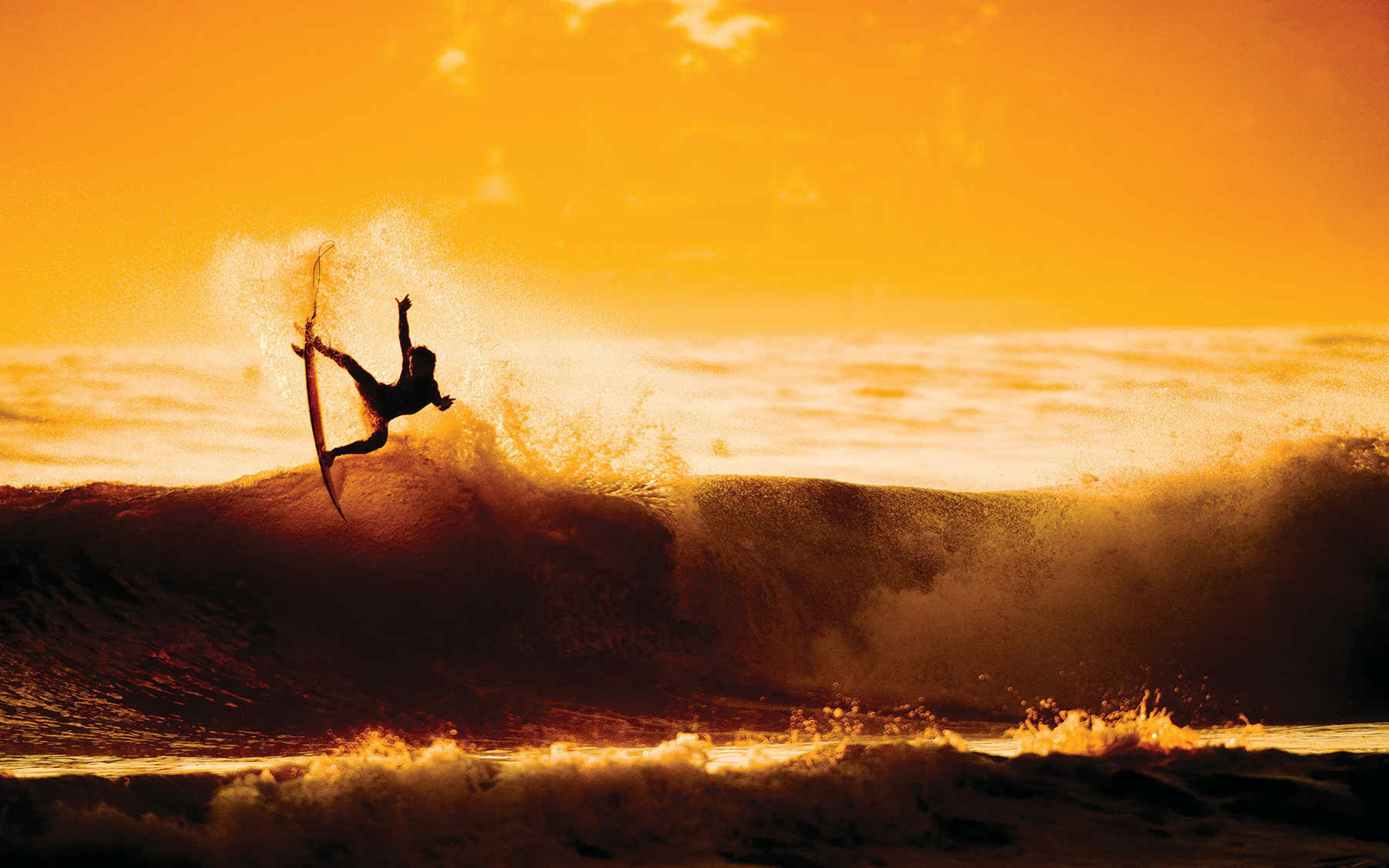 Silhouette of a surfer performing an aerial maneuver on a wave during sunset, Surfing Wallpaper