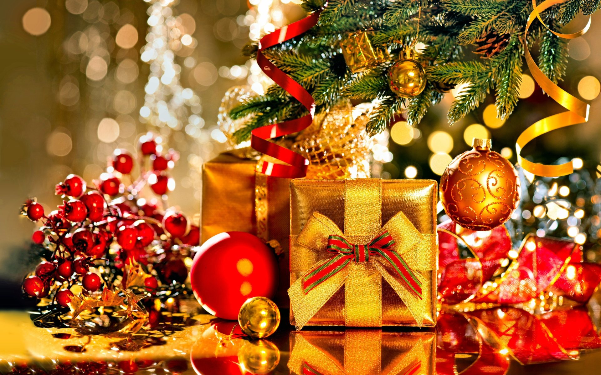 Glittering gold and red Christmas ornaments, gifts, and ribbons arranged under a decorated Christmas tree with twinkling lights in the background
