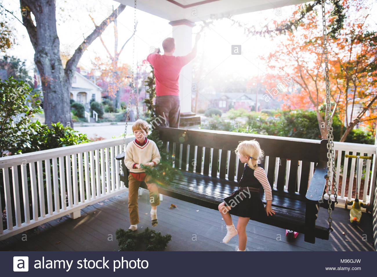 Kids Sitting On Swinging Bench With Man In Background Stock Photo