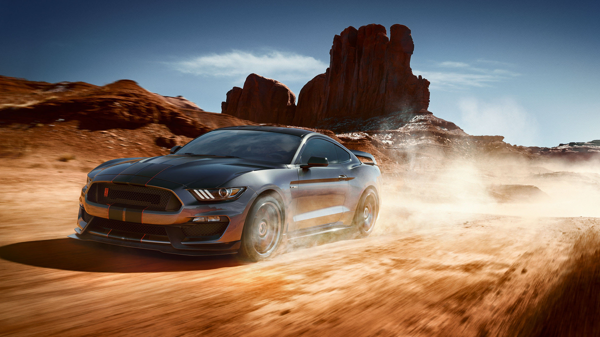 A gray Ford Mustang Shelby GT350 races through a desert landscape, kicking up dust