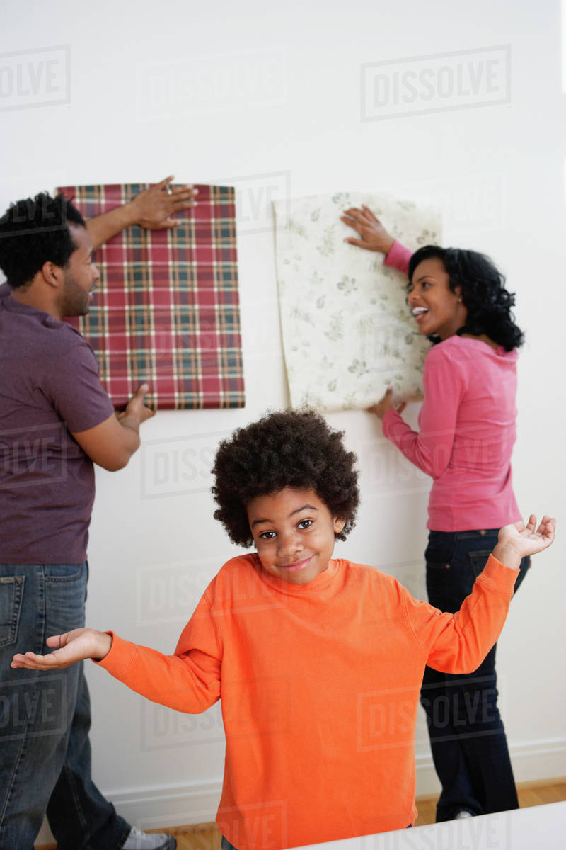 African Boy Shrugs While Parents Choose Wallpaper Stock Photo