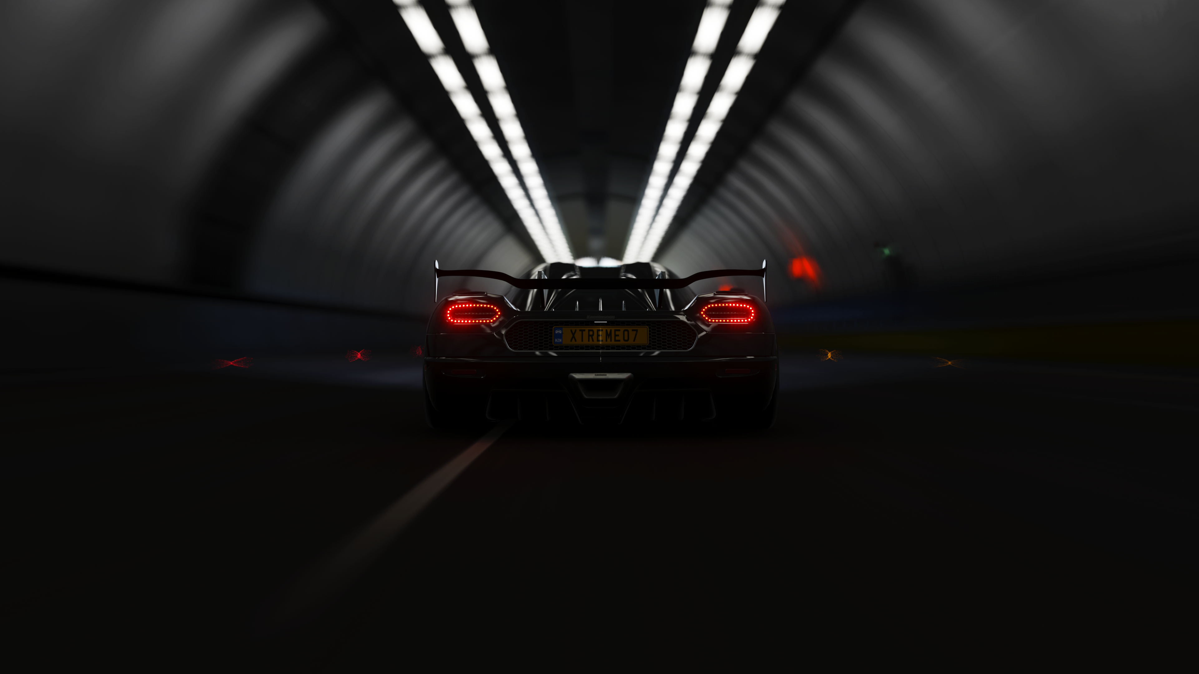 A rear view of a black Koenigsegg driving through a dimly lit tunnel, its taillights glowing red