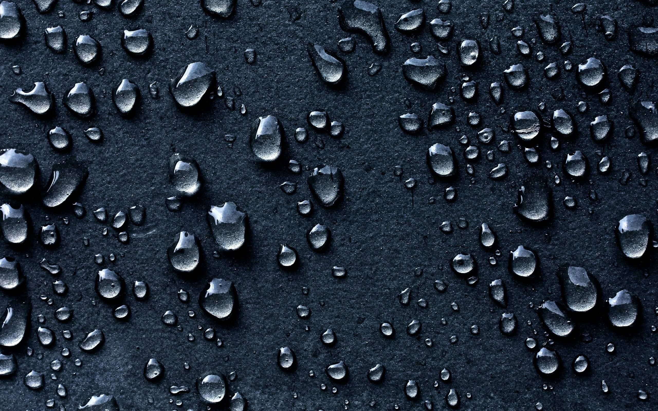 Close-up of water droplets on a dark, textured surface, creating a moody and abstract background