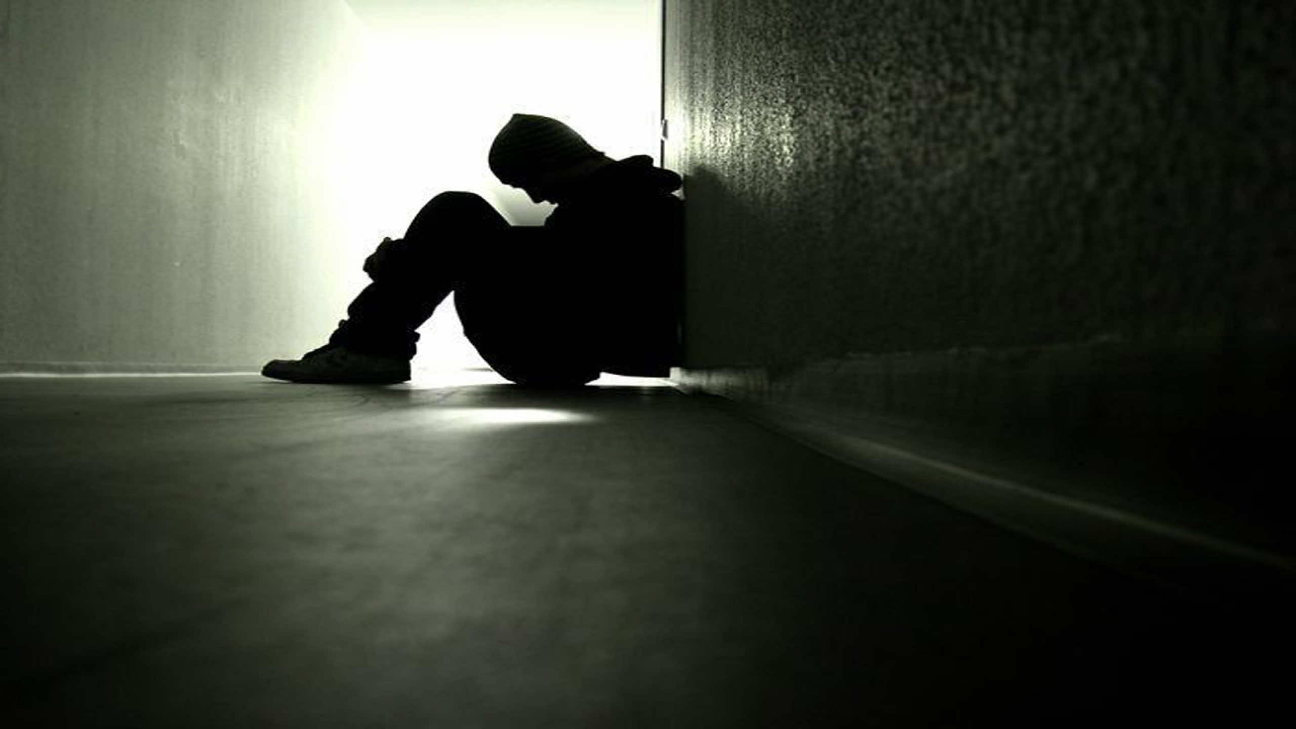 A silhouette of a person sitting alone in a dimly lit hallway, conveying feelings of sadness, loneliness, and isolation