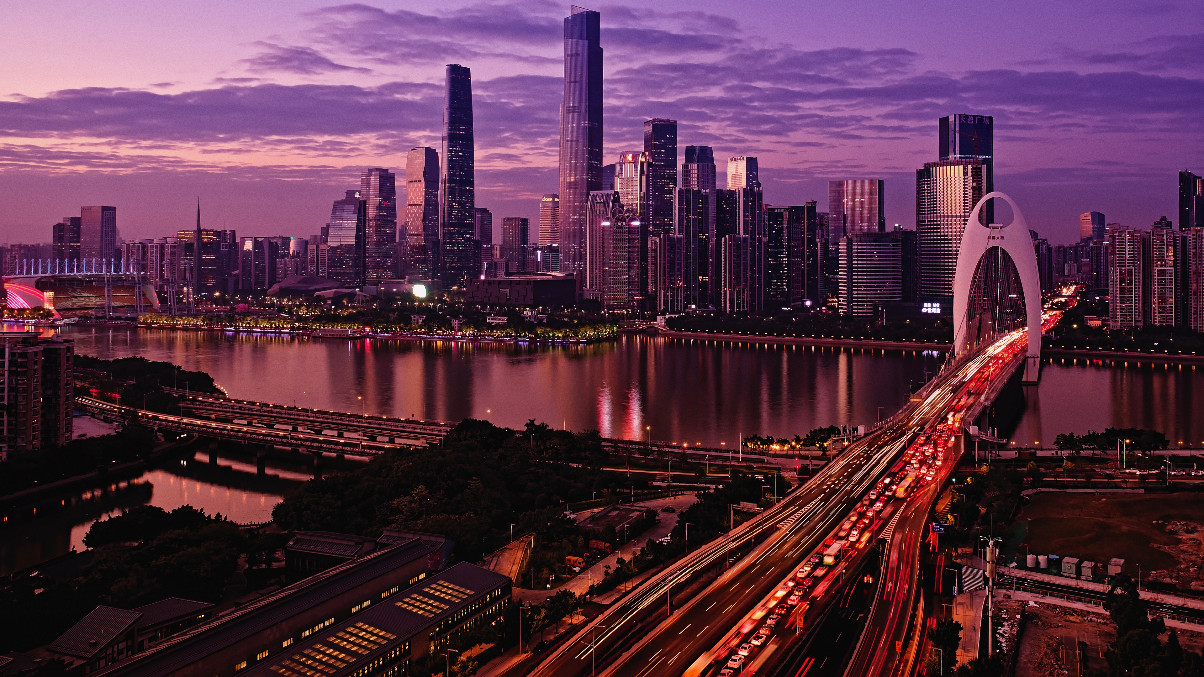 A breathtaking cityscape of Guangzhou illuminated at sunset, featuring Liede Bridge over the Pearl River, reflecting purple hues in the tranquil waters