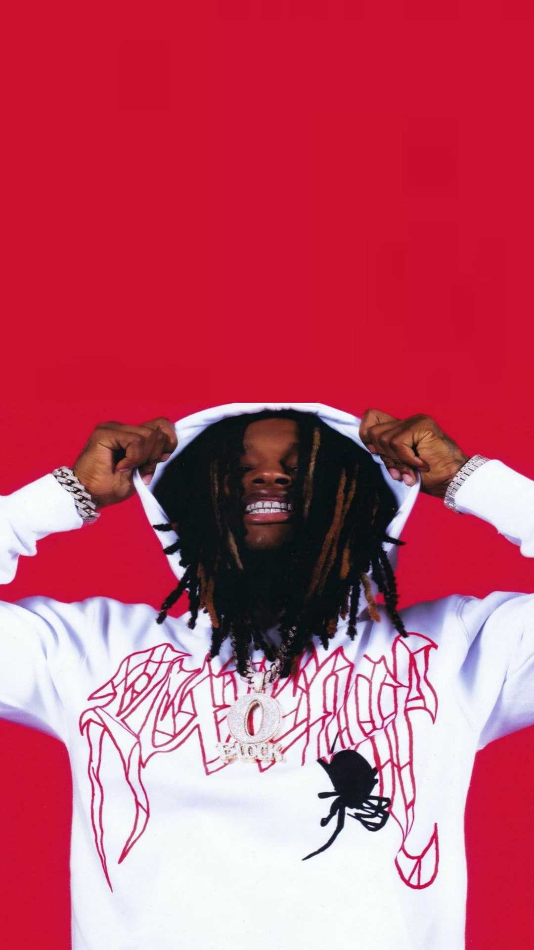 A rapper wearing a white hoodie with red designs and a large pendant against a red background