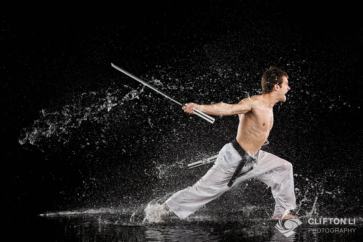 Martial artist performing a dynamic kata with a bo staff amidst splashing water