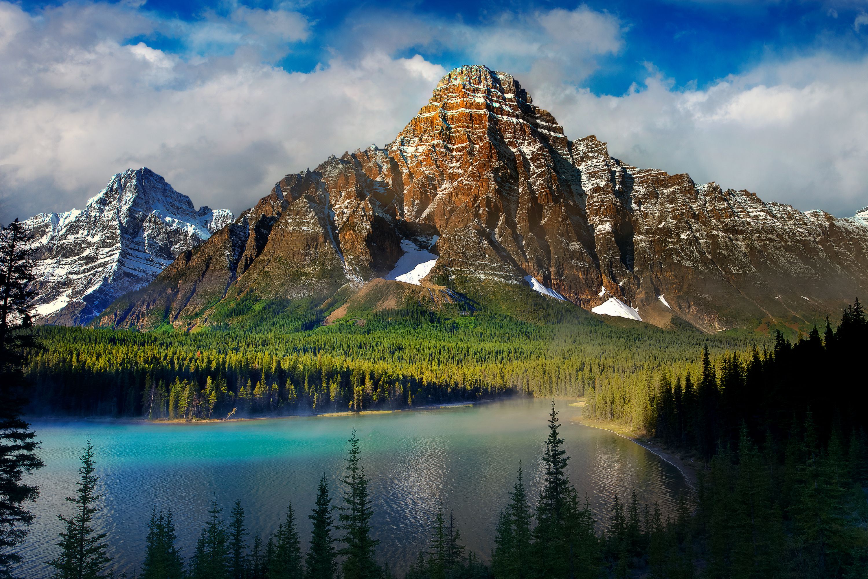 Scenic 4k wallpaper of a majestic mountain range with snow-capped peaks reflected in a turquoise lake, surrounded by a lush green forest