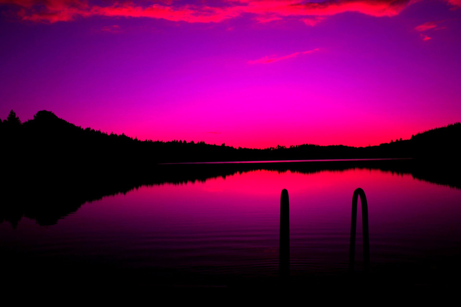 A stunning 4K wallpaper featuring a vibrant pink and purple sunset over a calm lake, with the silhouettes of trees along the shoreline and a dock in the foreground