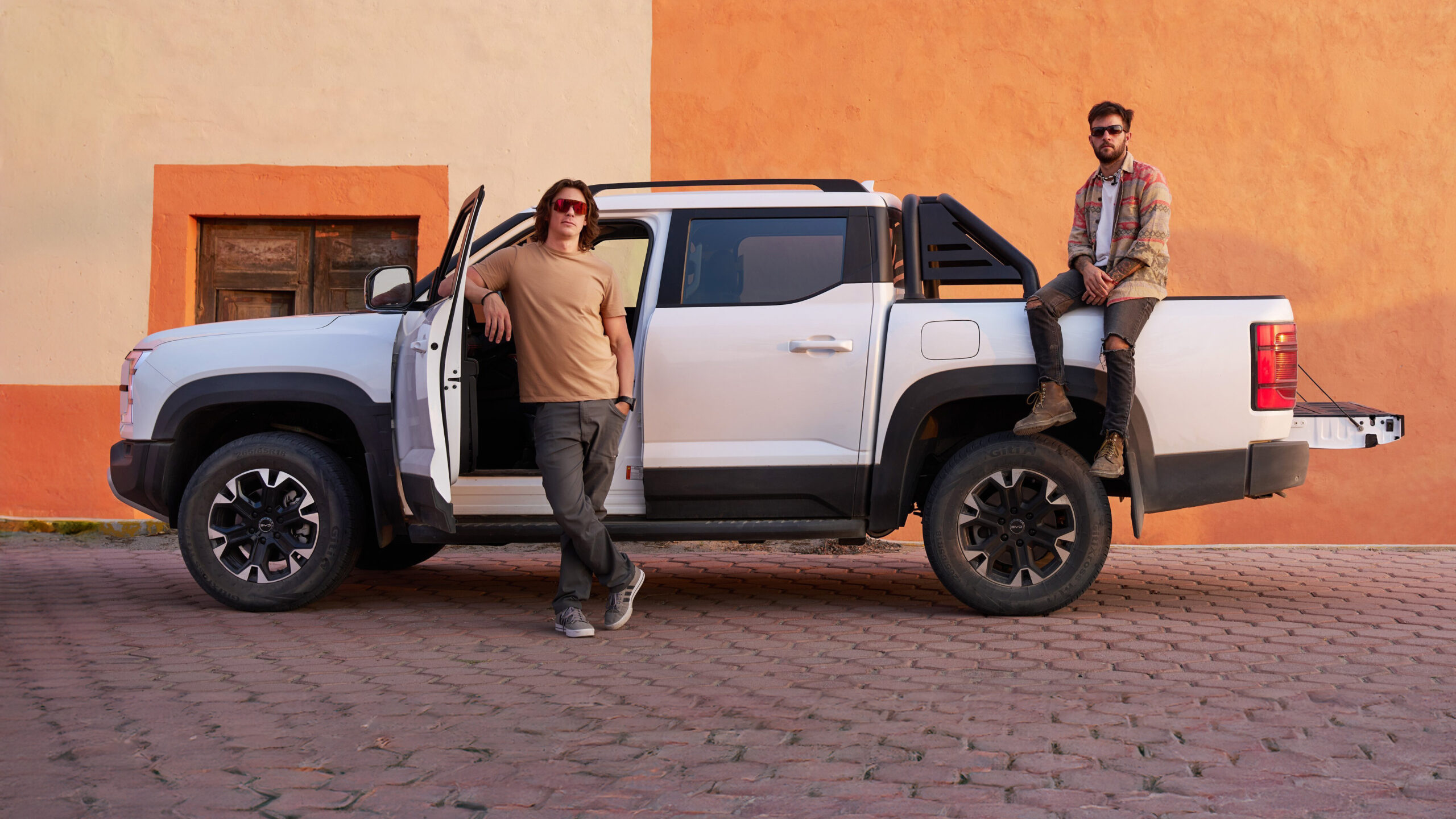Two men standing next to a white BYD pickup truck parked against an orange and tan wall
