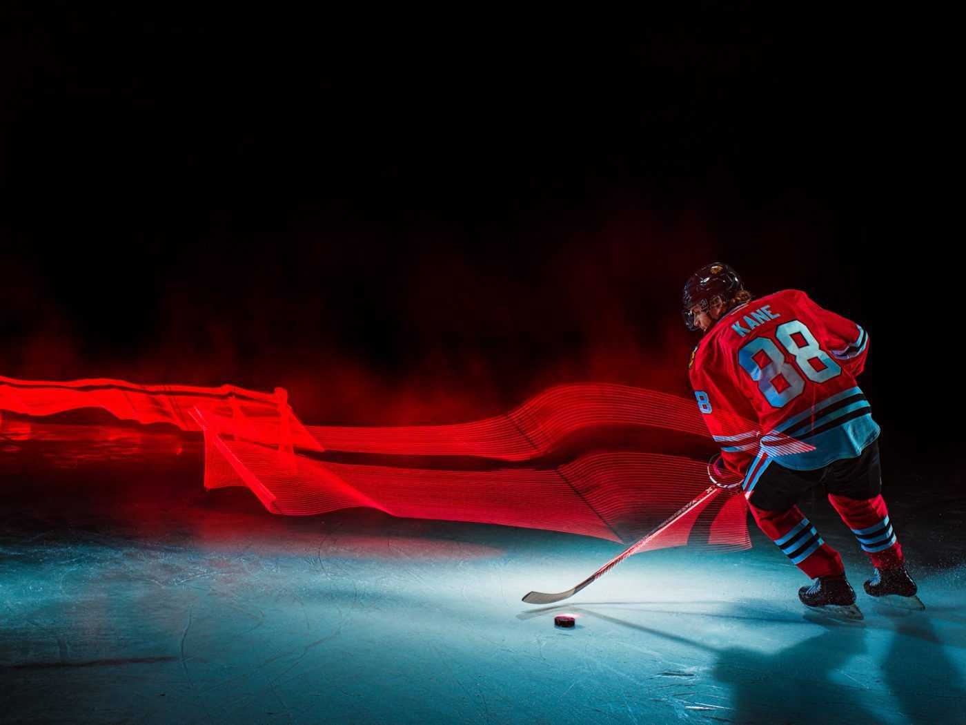 Action shot of a hockey player in a red and blue jersey with the number 88, skating on an ice rink with dynamic red light trails in the background