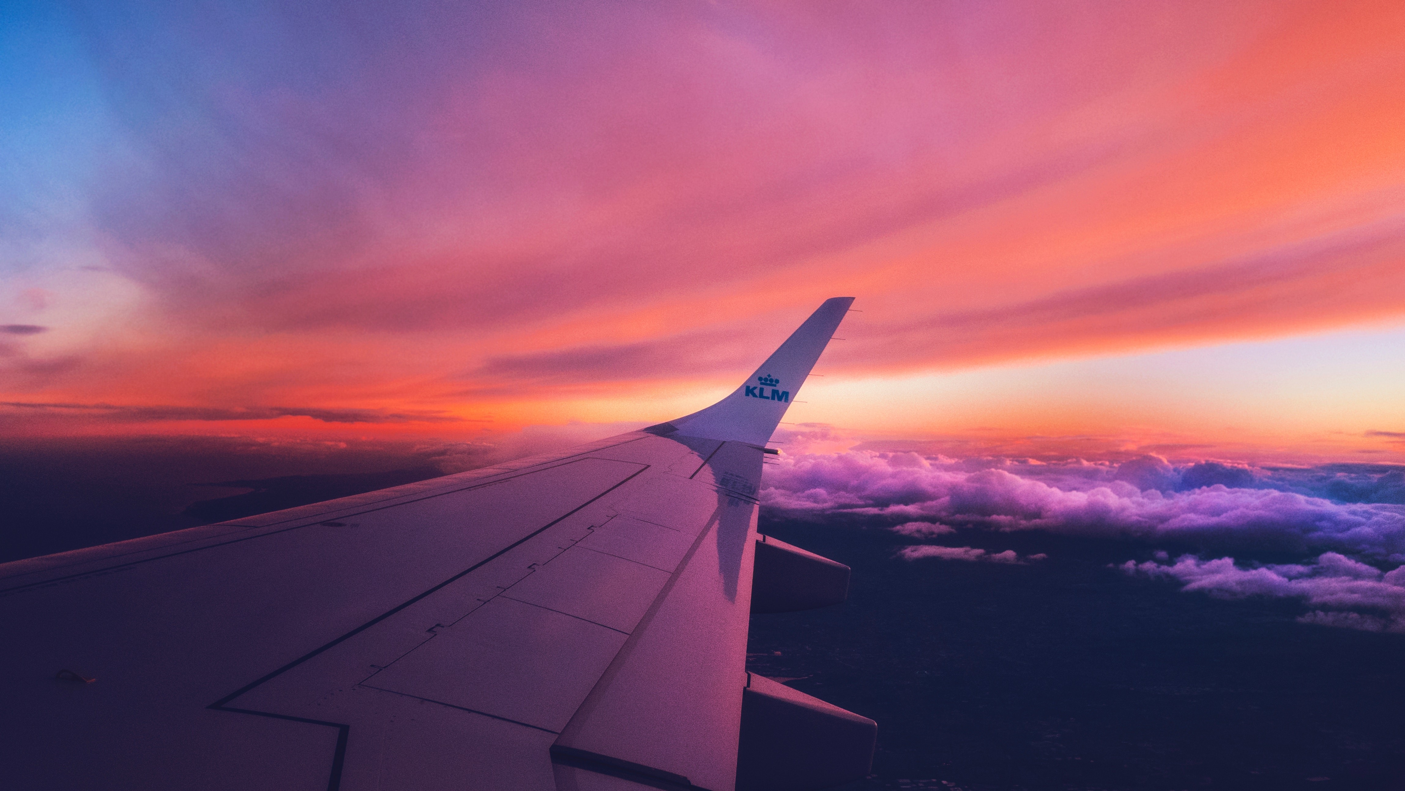 Airplane wing soaring through a vibrant sunset sky, with a breathtaking view of the clouds below
