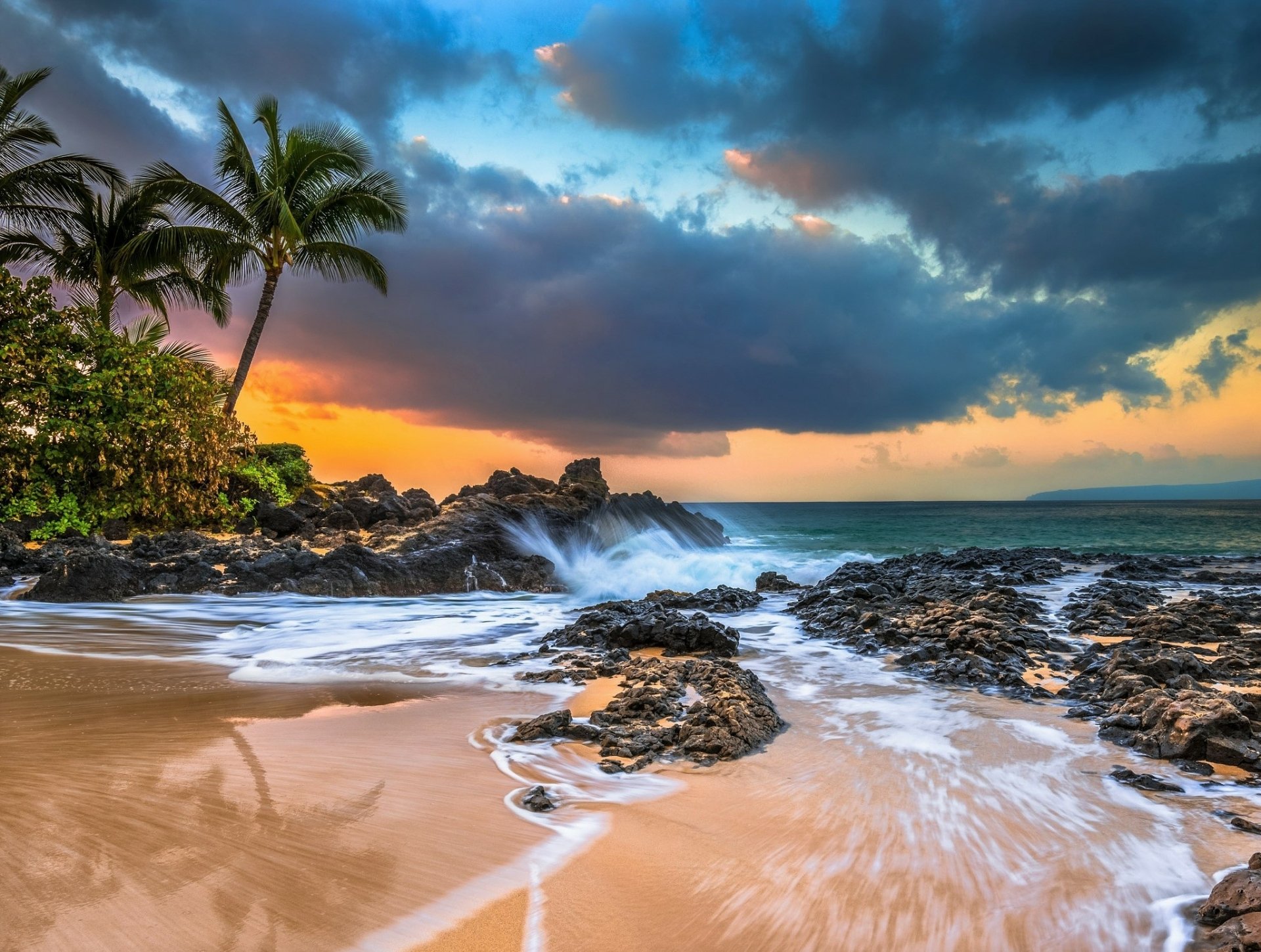 A breathtaking Hawaiian beach at sunset with palm trees, volcanic rocks, and waves crashing on the shore. Perfect for a desktop background