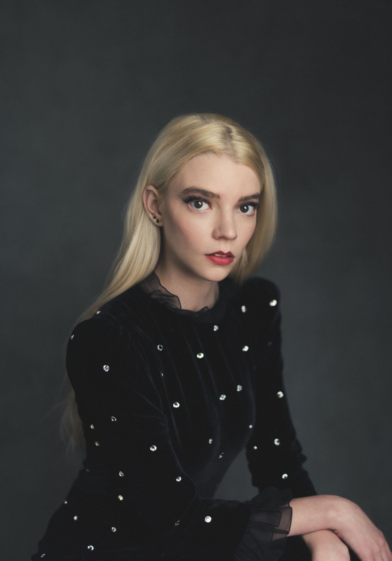 Anya Taylor-Joy in a black velvet dress with rhinestone embellishments, posing against a dark background