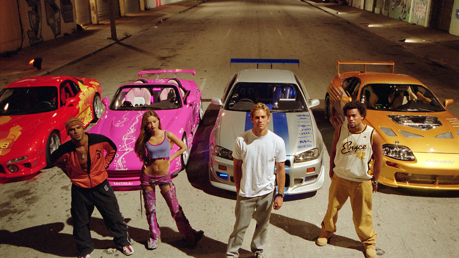 The main cast of The Fast and the Furious posing with their iconic cars