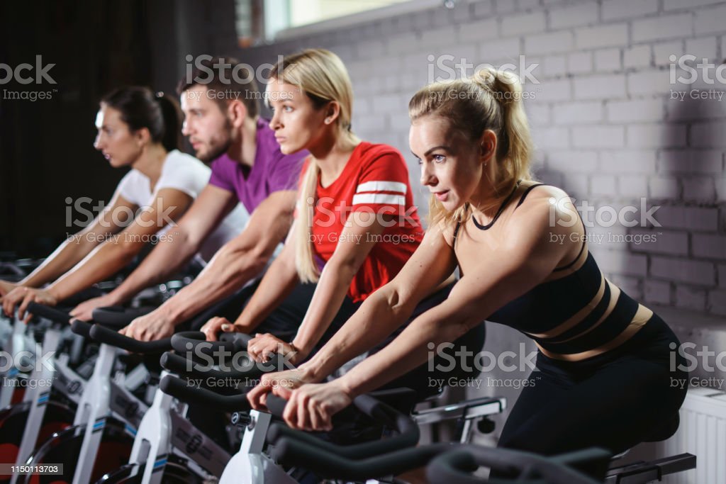 Group Of Smiling Friends At Gym Exercising On Stationary Bike