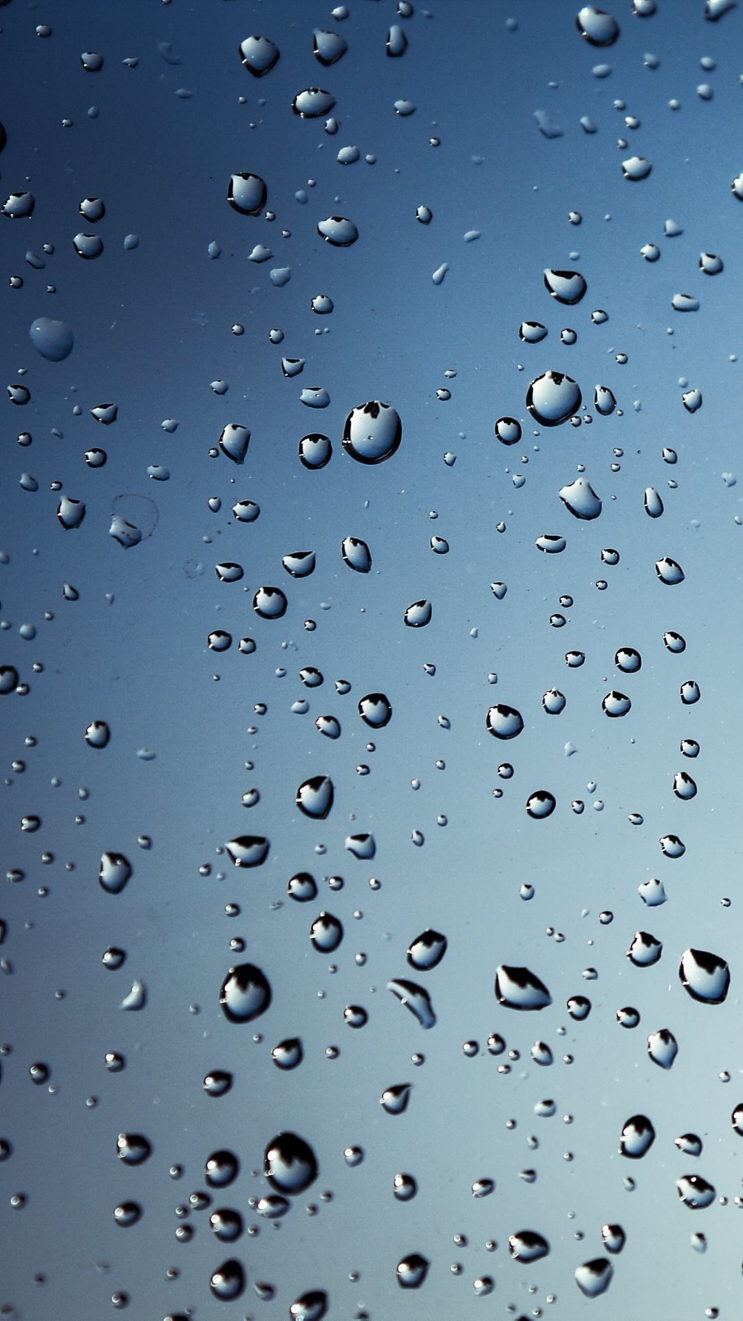 Close-up of raindrops on a window, creating a textured pattern against a soft blue background
