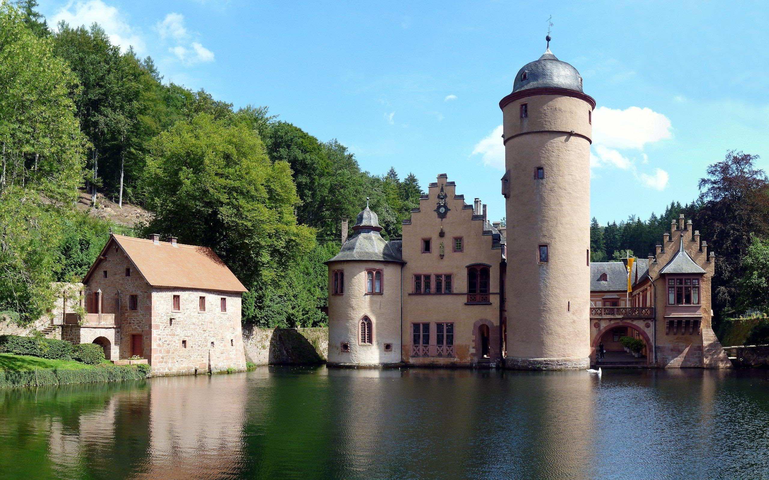 A picturesque view of Mespelbrunn Castle, a medieval castle in Germany, surrounded by a moat and lush greenery