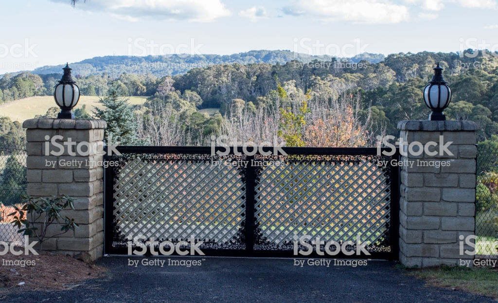 Metal Driveway Entrance Gates Set In Brick Fence With Garden Trees