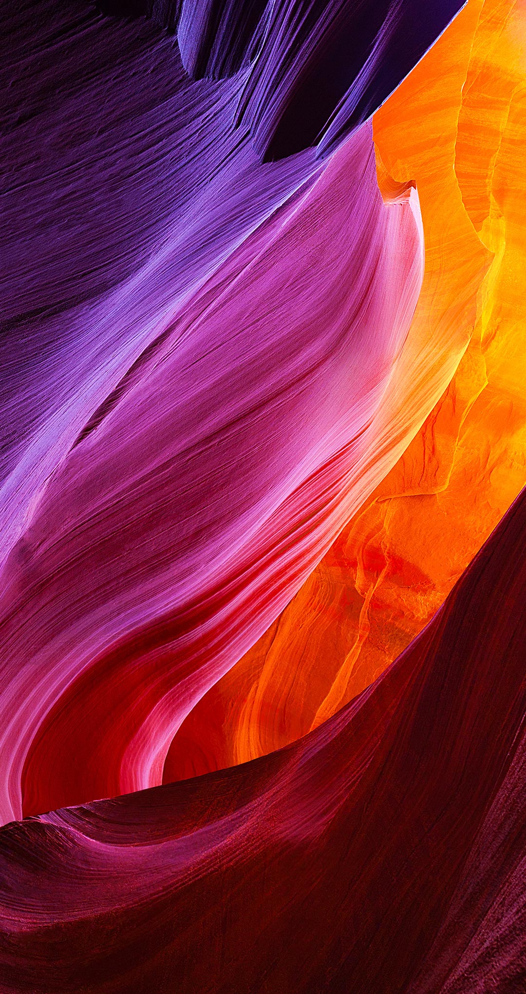 Vivid colors blend together seamlessly in this abstract wallpaper, showcasing the smooth lines and curves of a sandstone canyon. The hues transition from deep purples and magentas to fiery oranges and reds, creating a mesmerizing visual experience