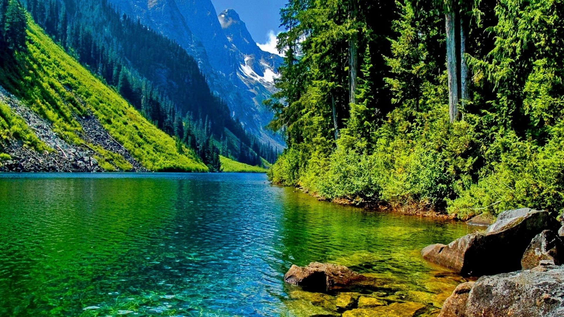 A stunning landscape photograph of a pristine lake nestled amidst a mountain valley. The clear, turquoise water reflects the surrounding lush green forest and snow-capped peaks, creating a breathtaking natural scene