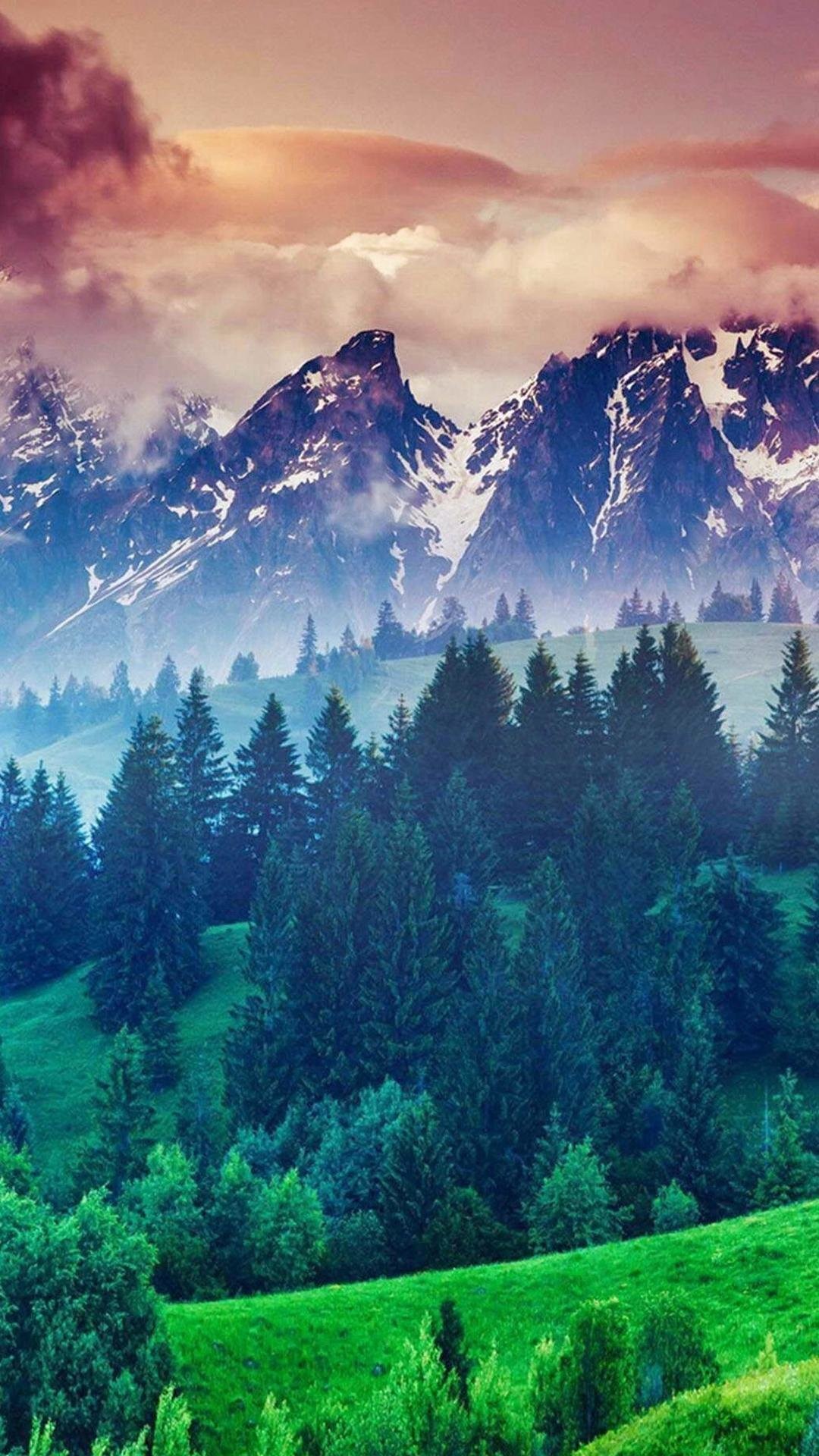 Lush green hills rolling beneath majestic snow-capped mountains under a vibrant sunset sky