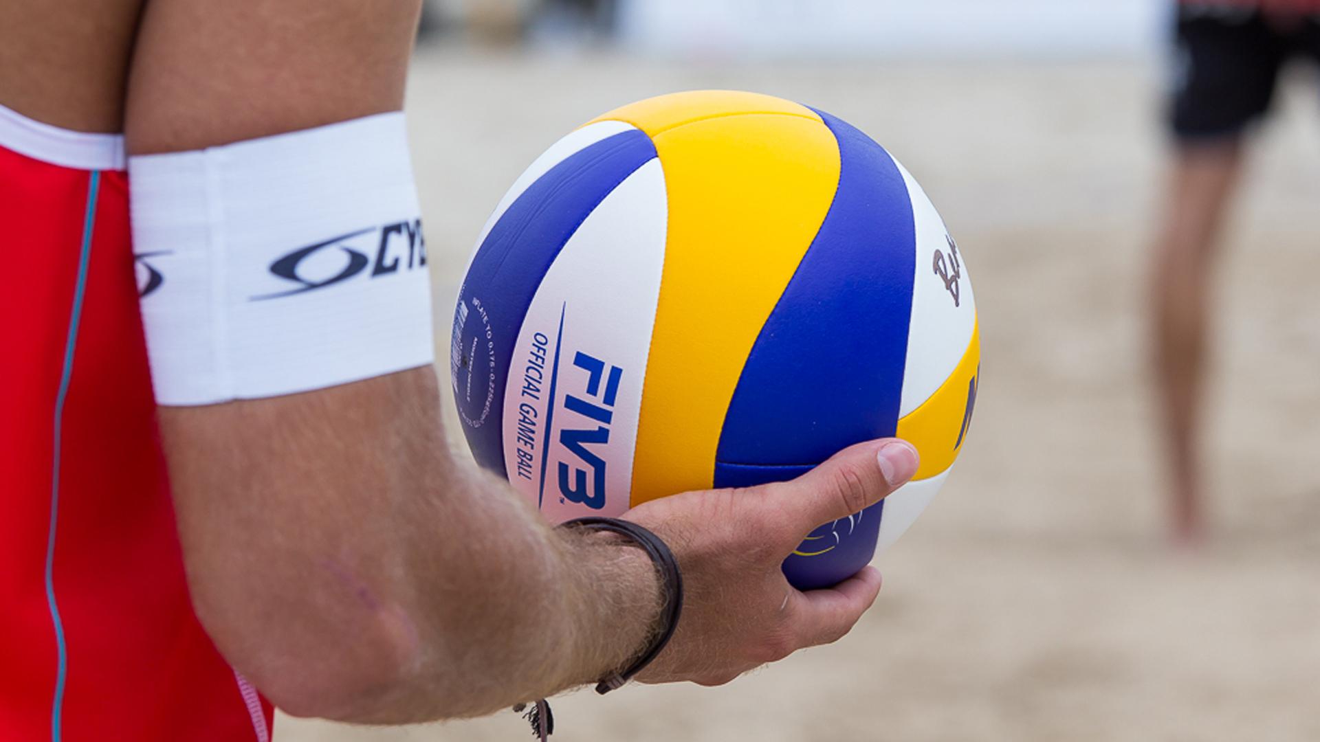 A close-up of a volleyball player's arm holding a brightly colored beach volleyball, with the FIVB logo clearly visible