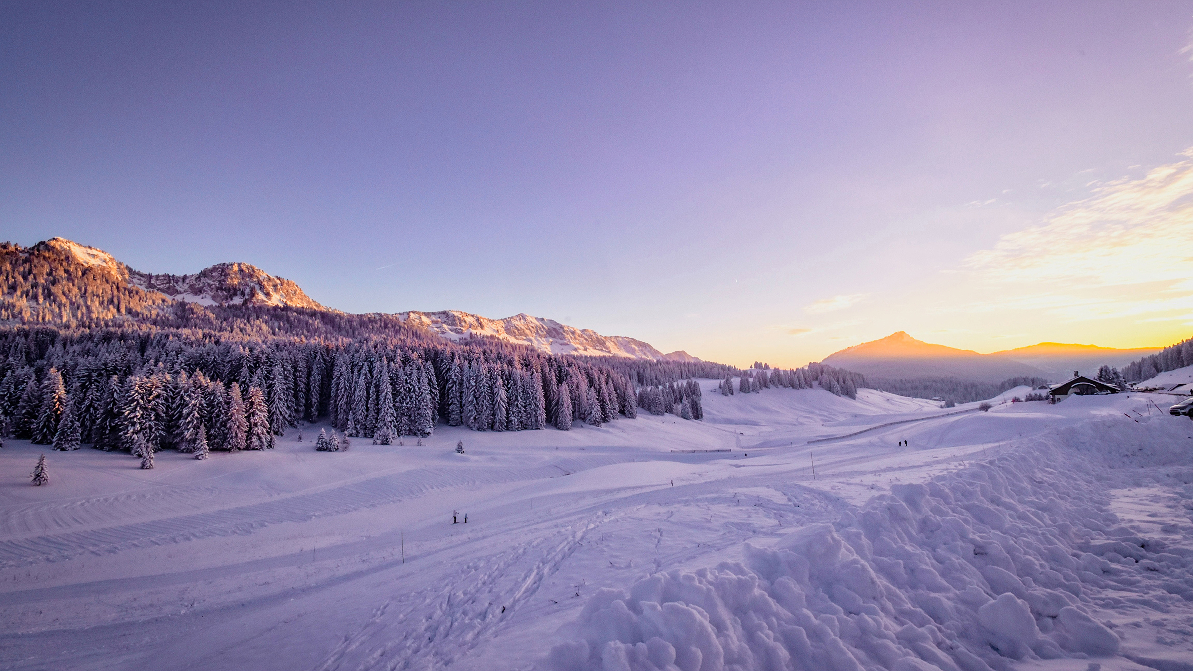 A breathtaking 4k wallpaper capturing a snow-covered valley at sunset, with a pristine ski slope winding through frost-covered trees and distant mountains bathed in golden light