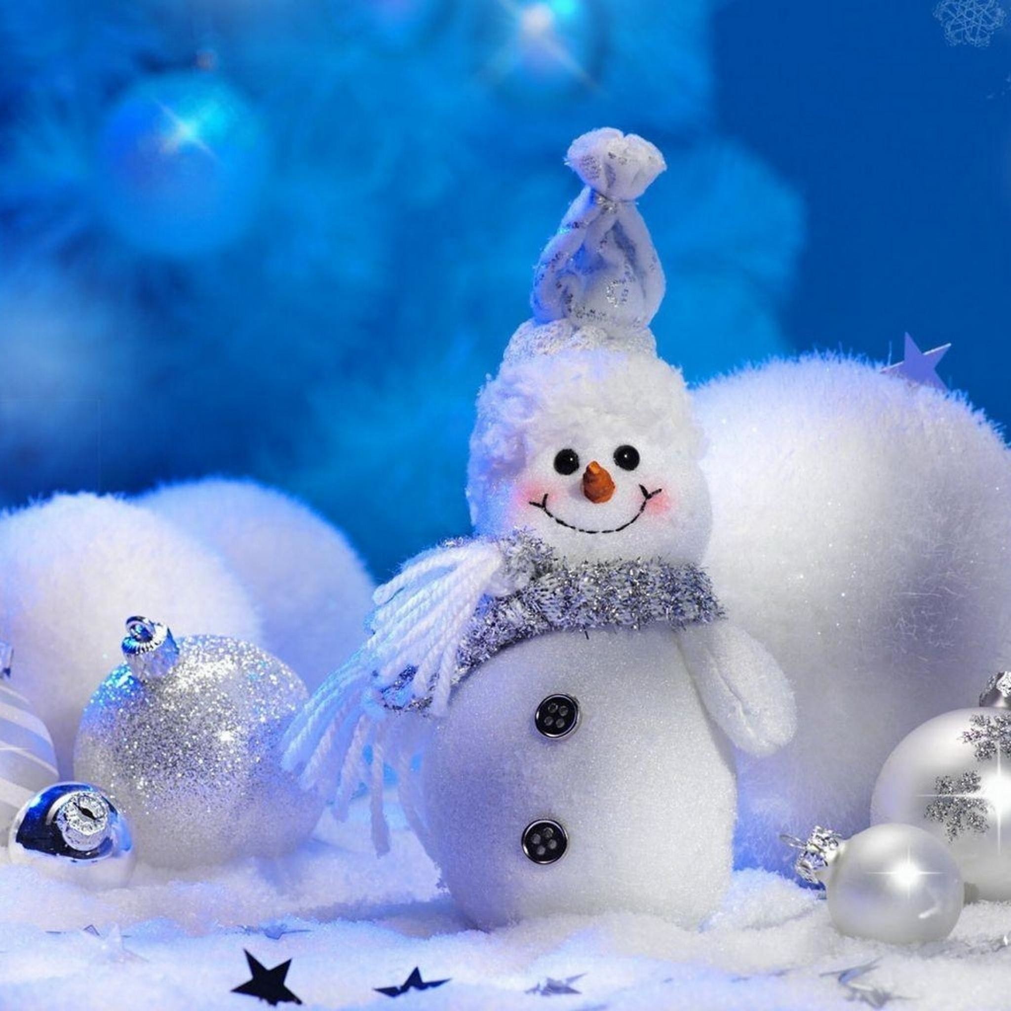 A cheerful snowman figurine sits amidst sparkling silver ornaments and fluffy snowballs, against a backdrop of a glowing blue Christmas tree