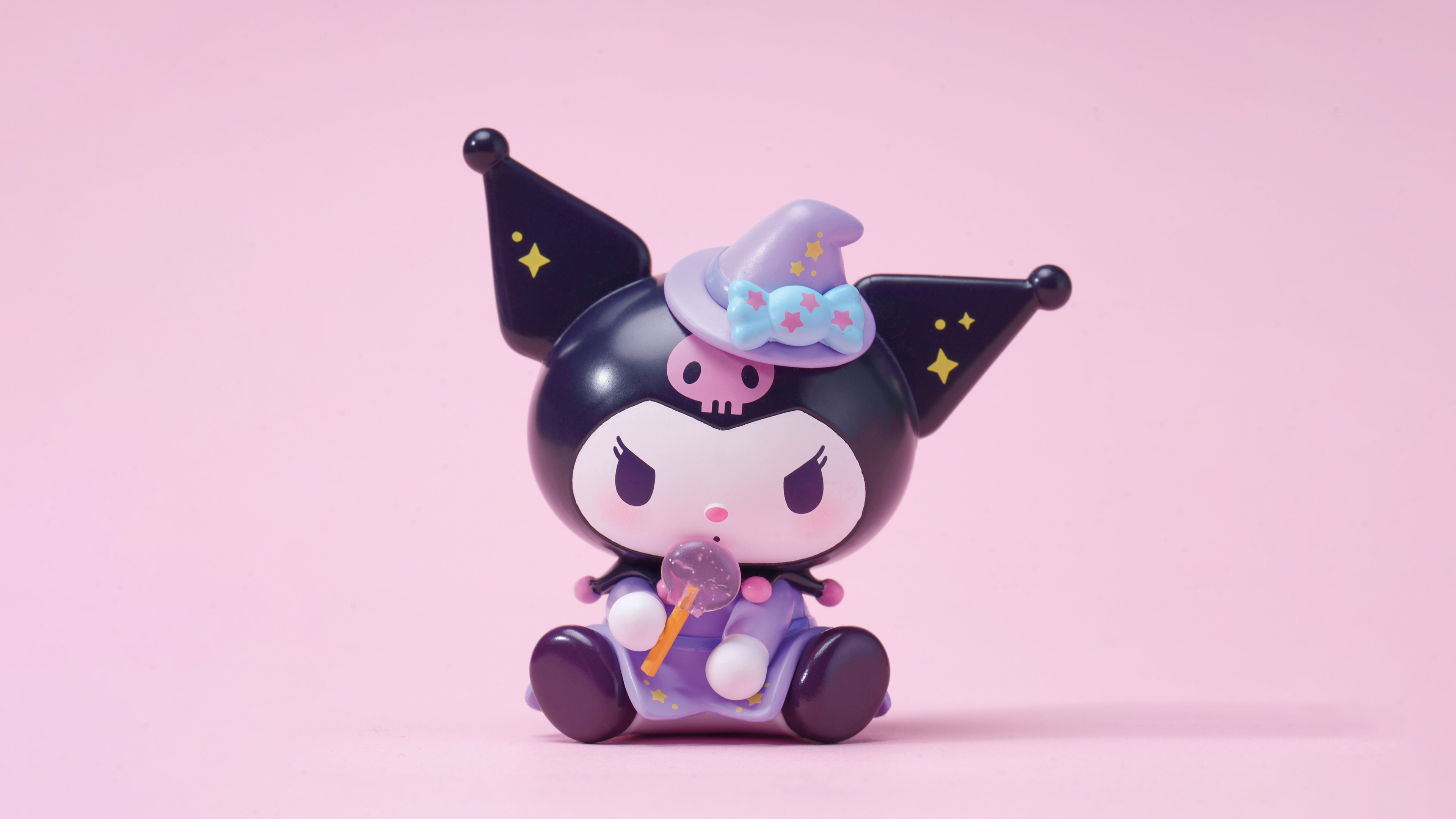 Kuromi dressed as a witch, holding a lollipop, on a pink background